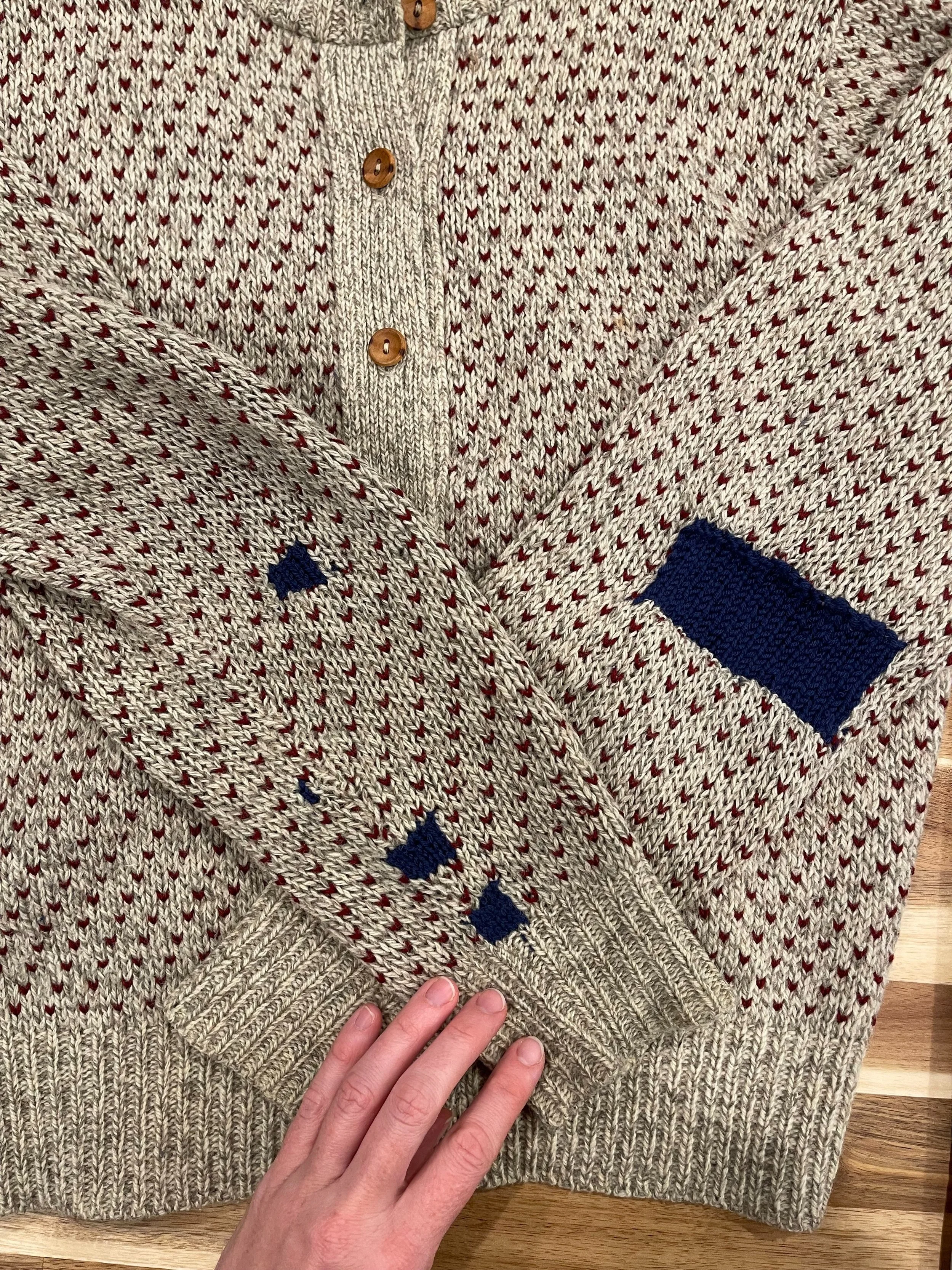 A grey and maroon sweater mended with dark blue yarn.
