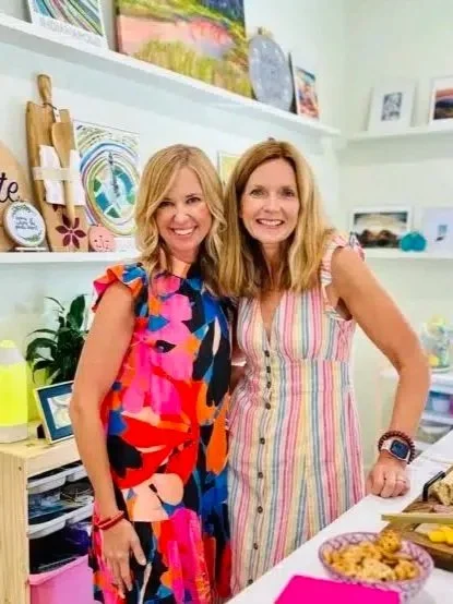 Two woman stand in an art studio, smiling.