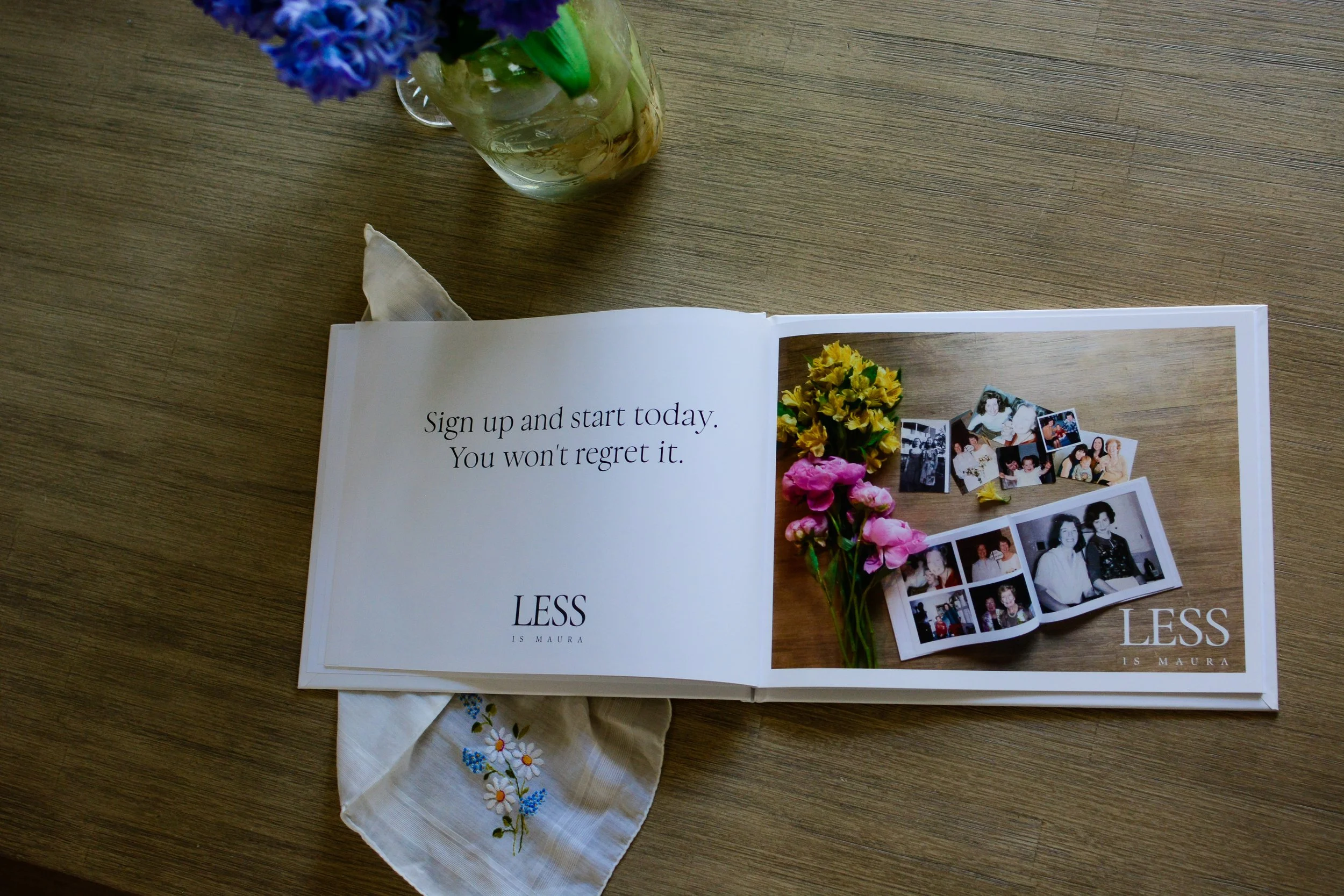 Looking down from above on a photo album with a picture and a description of instructions, lying open on a table with a vase of flowers and a handkerchief.