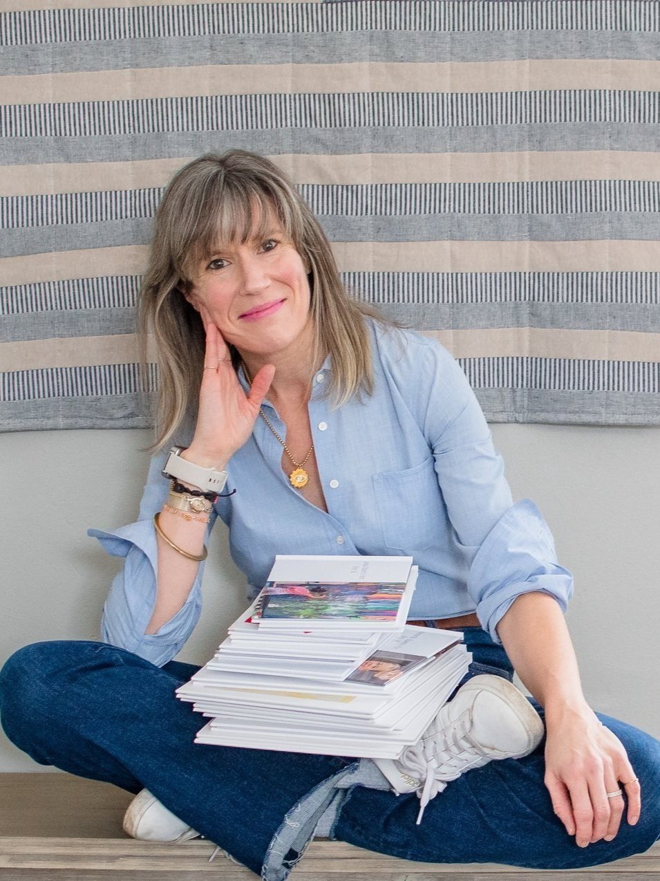 A woman sits criss cross applesauce on a bench with a stack of albums on her lap.