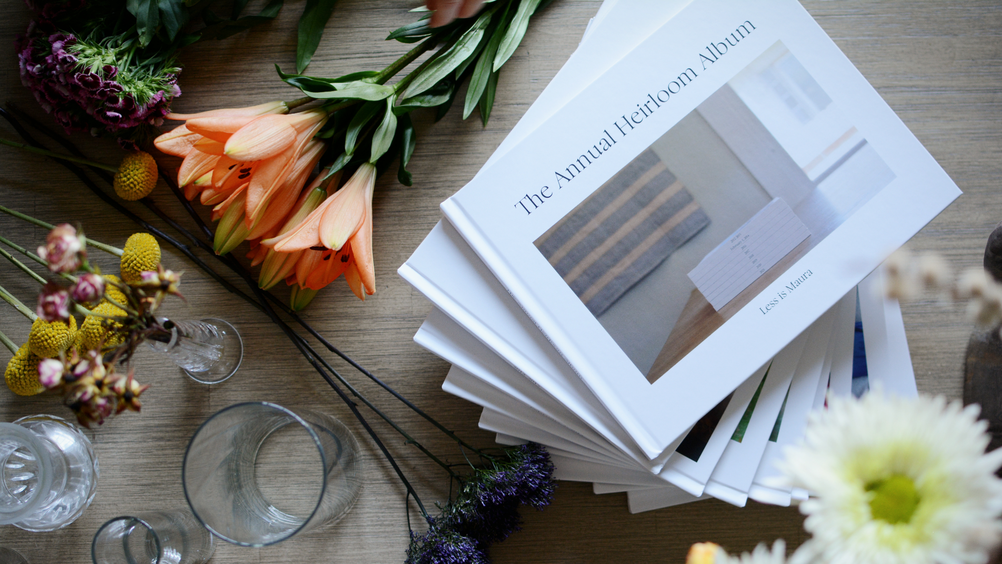 A stack of photo albums sits on a table next to flowers and vases.