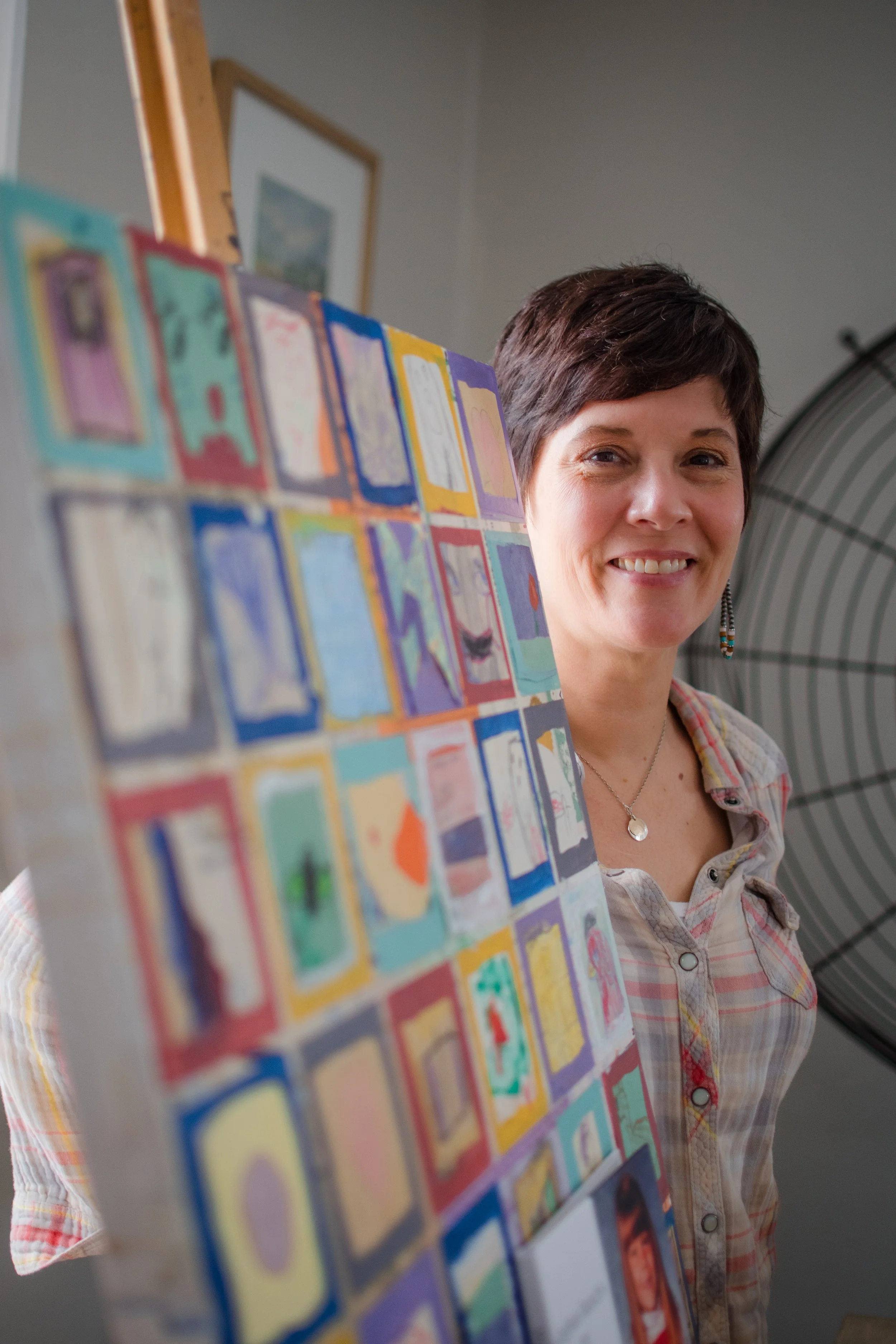 Meghan smiles into the camera, standing next to a piece of her artowrk.