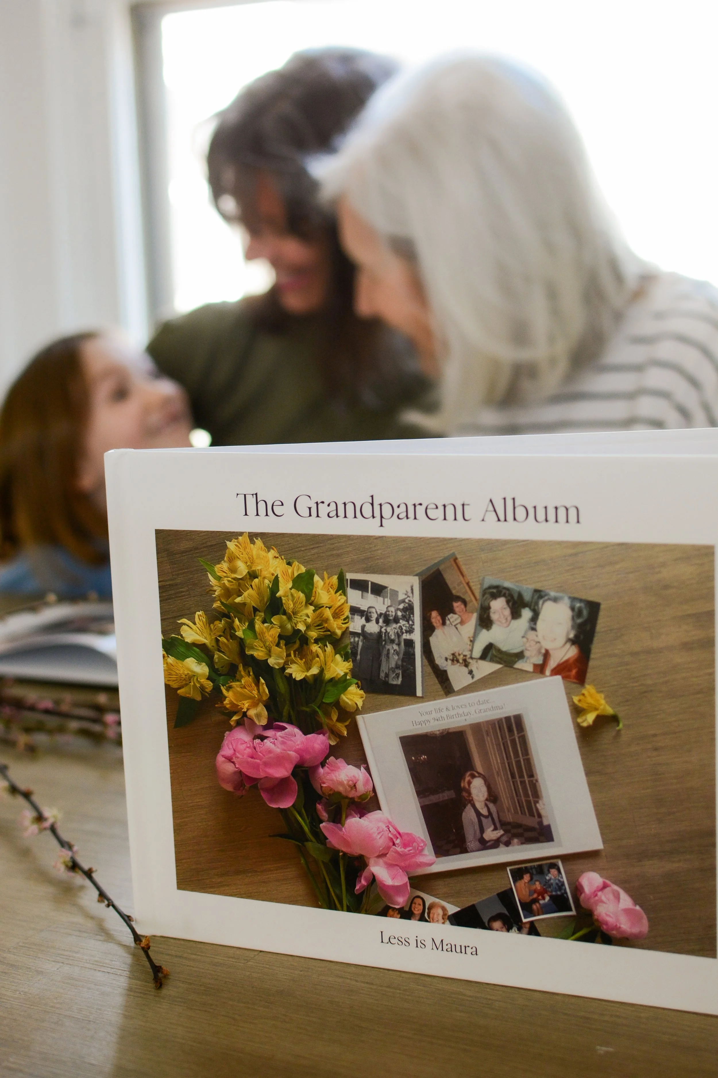 A photo album stands stands propped up with a grandma, mother and daughter laughing in the background.