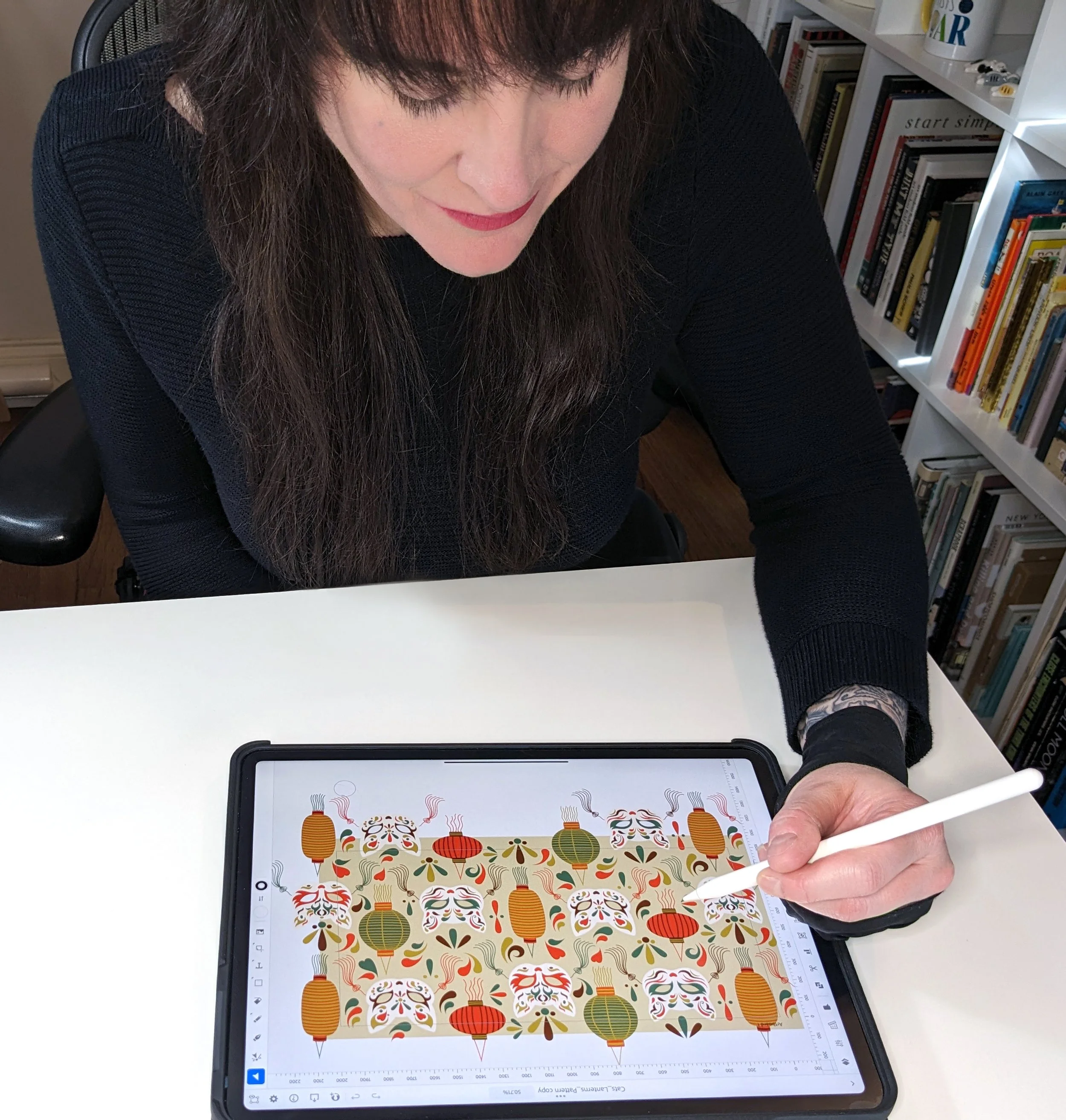 Woman using a stylus on a tablet displaying a colorful, decorative pattern with lanterns and abstract shapes.
