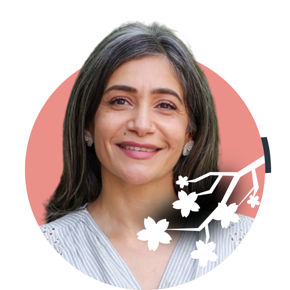 Thumbnail image of associate therapist Shabana Omar: A woman with shoulder-length dark gray hair smiling, wearing earrings and a light striped blouse with a dark background and a pink cherry blossom branch graphic.