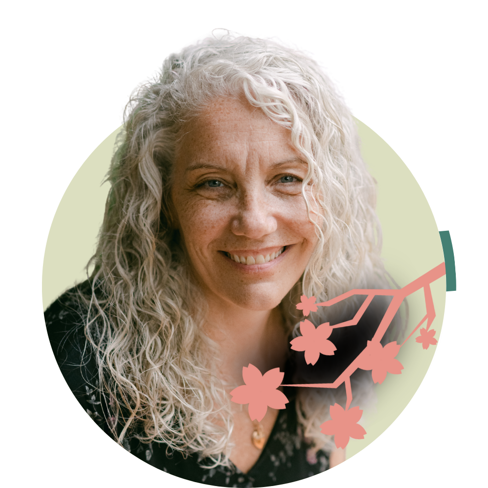 Thumbnail image of associate therapist Beth Lewis: A smiling woman with curly gray hair, wearing a black top with a floral pattern, and a necklace, against a light background with a pink cherry blossom illustration.