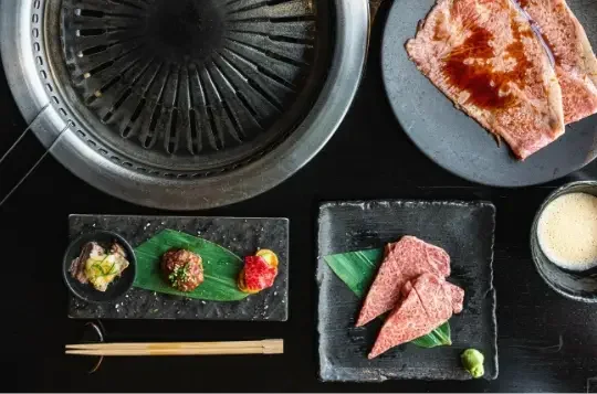 Japanese barbecue grill with raw beef slices, dipping sauces, chopsticks, and a small plate of meat and vegetables.