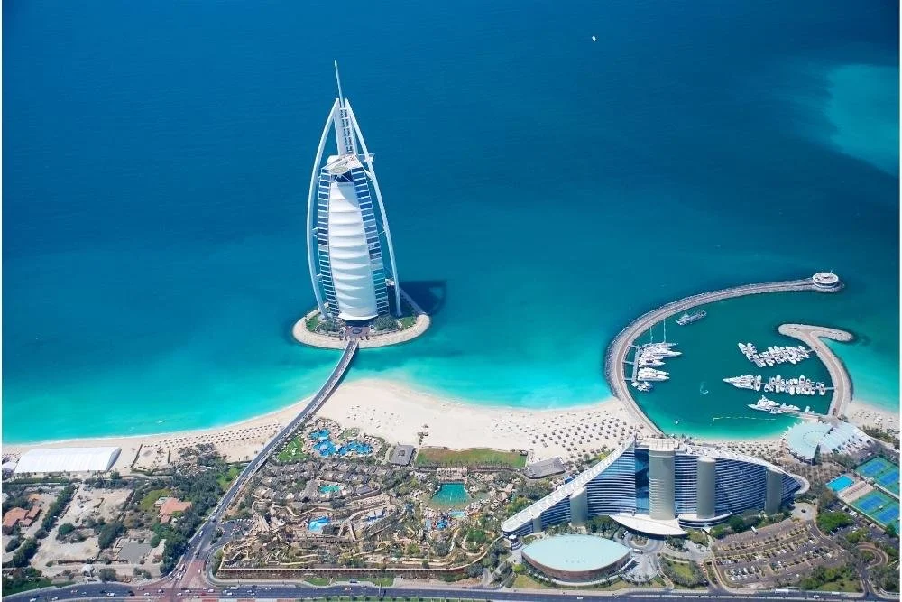 Aerial view of the Atlantis Paradise Island resort and the Burj Al Arab hotel on a turquoise ocean, with a sandy beach and marina with boats.