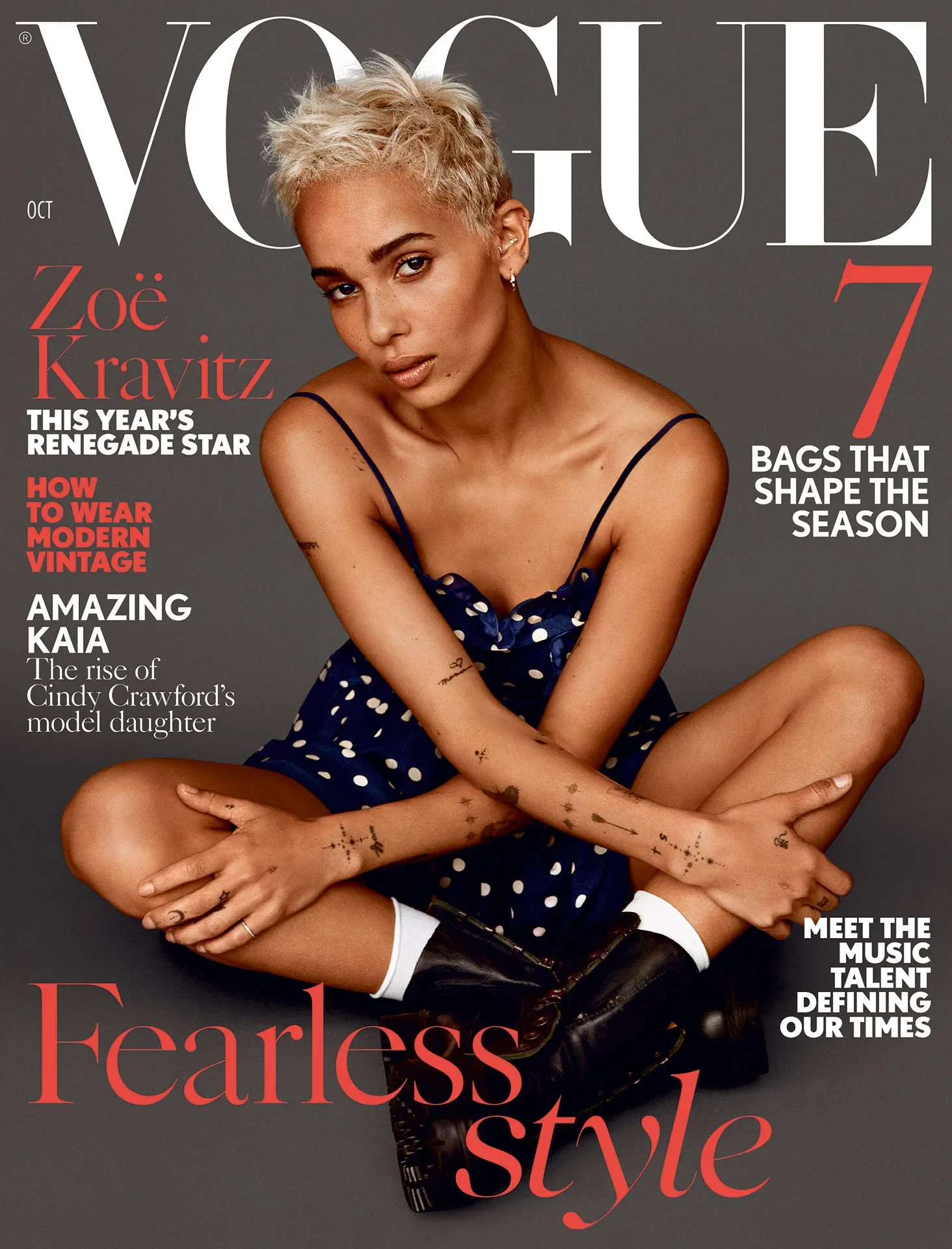 Vogue magazine cover featuring Zoë Kravitz with short blonde hair, sitting cross-legged against a gray background, wearing a navy blue polka dot dress and black combat boots.