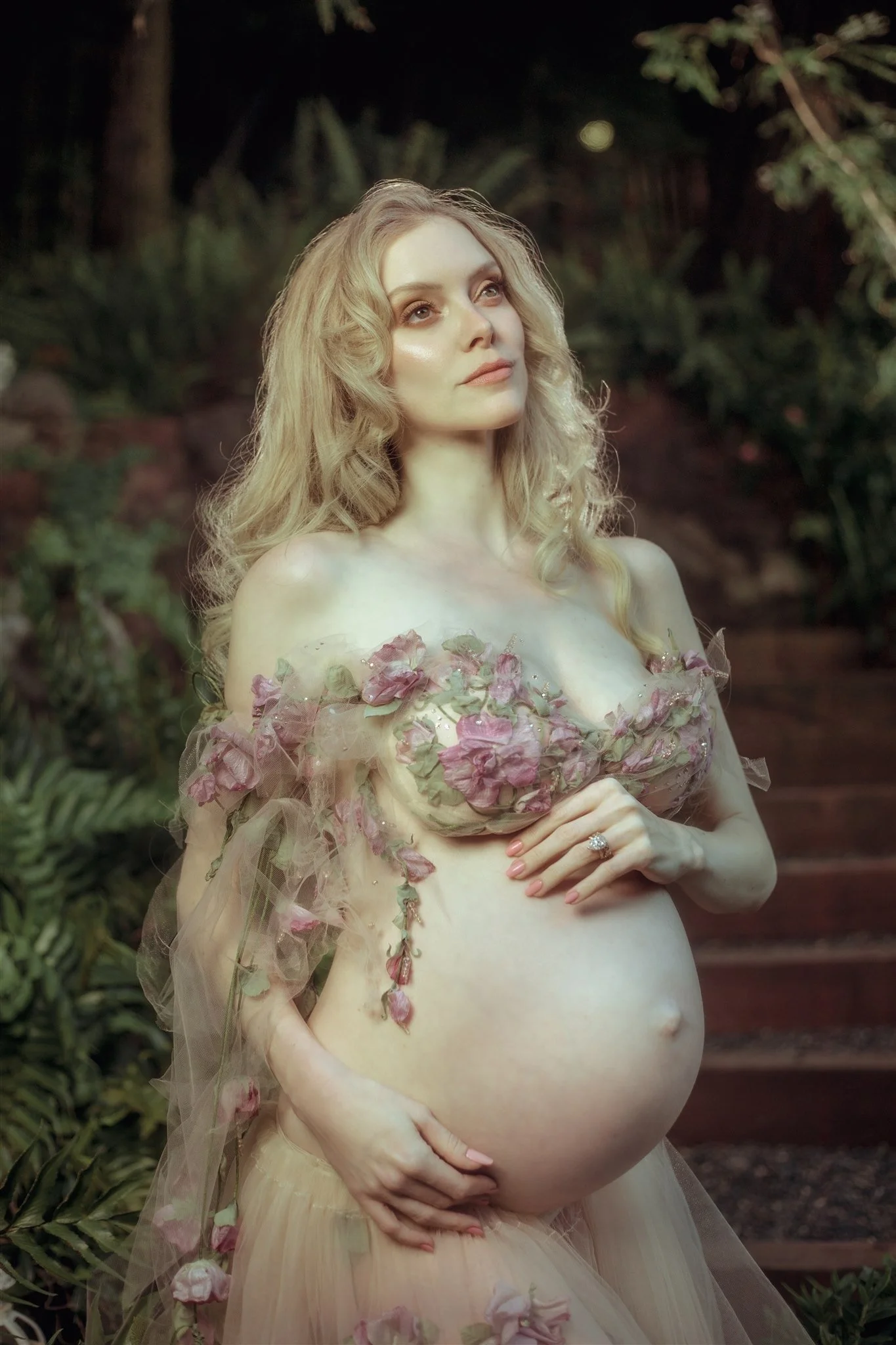 Pregnant woman in a floral dress standing outdoors in a garden.