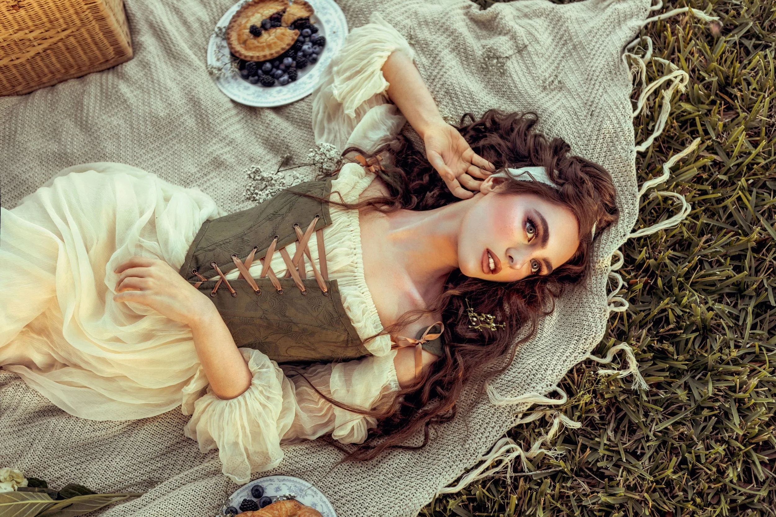 A woman lying on a blanket outdoors withberries and a plate of pastries nearby.
