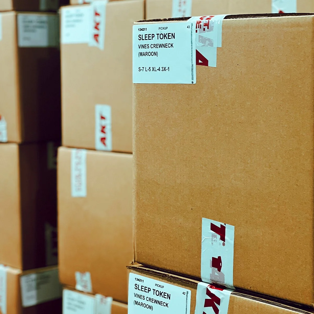 Stacked cardboard boxes with labels indicating 'SLEEP TOKEN Vines Crewneck (Maroon).'