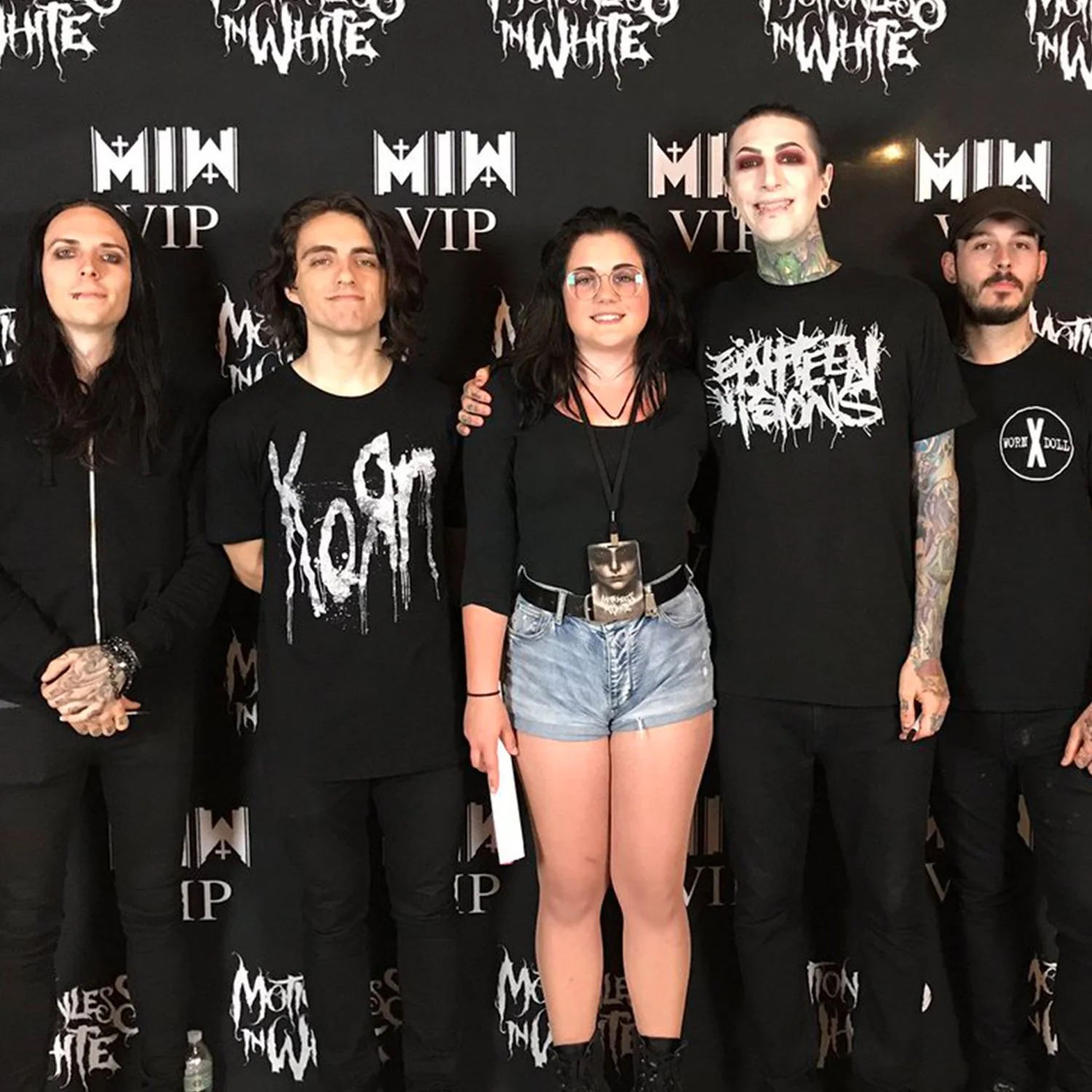 Group photo of four people with a fan at a Motionless In White VIP event, wearing black clothing, standing in front of a branded backdrop.