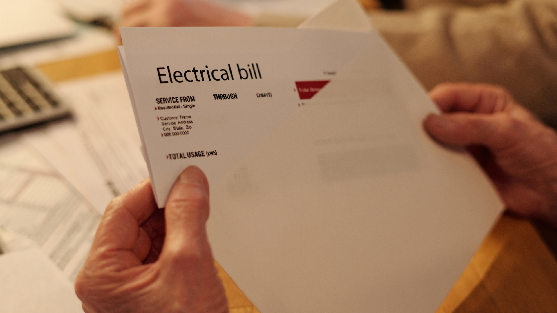 Person holding a past-due electric bill while looking over household expenses in Pensacola, Florida.