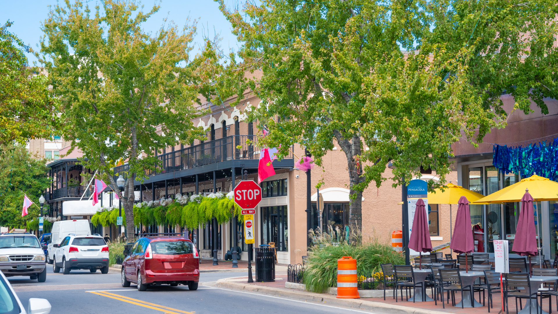 Downtown Pensacola street lined with local businesses, restaurants, trees, and outdoor seating.