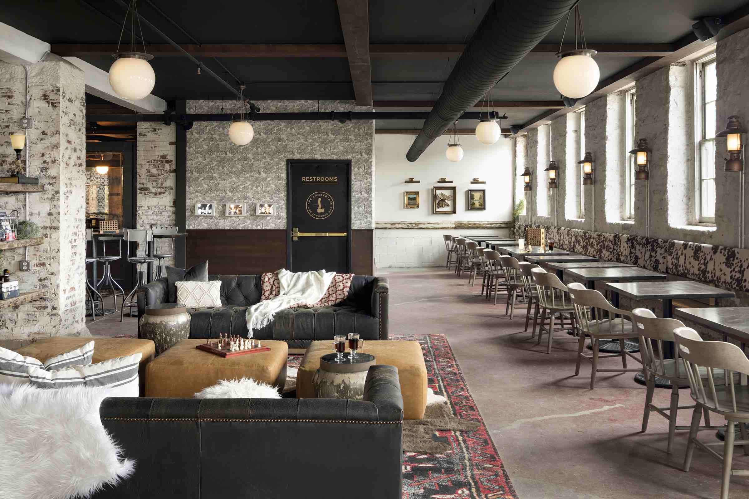 A long room with a dark wooden ceiling, a long row of tables and chairs and a lounge area with black and tan leather furniture
