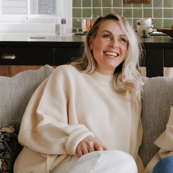 Regan Nix, co-founder of Minnesota architecture and interior design firm Blue Pencil Collective, sits on a gray couch in front of a white window laughing and pointing at the camera