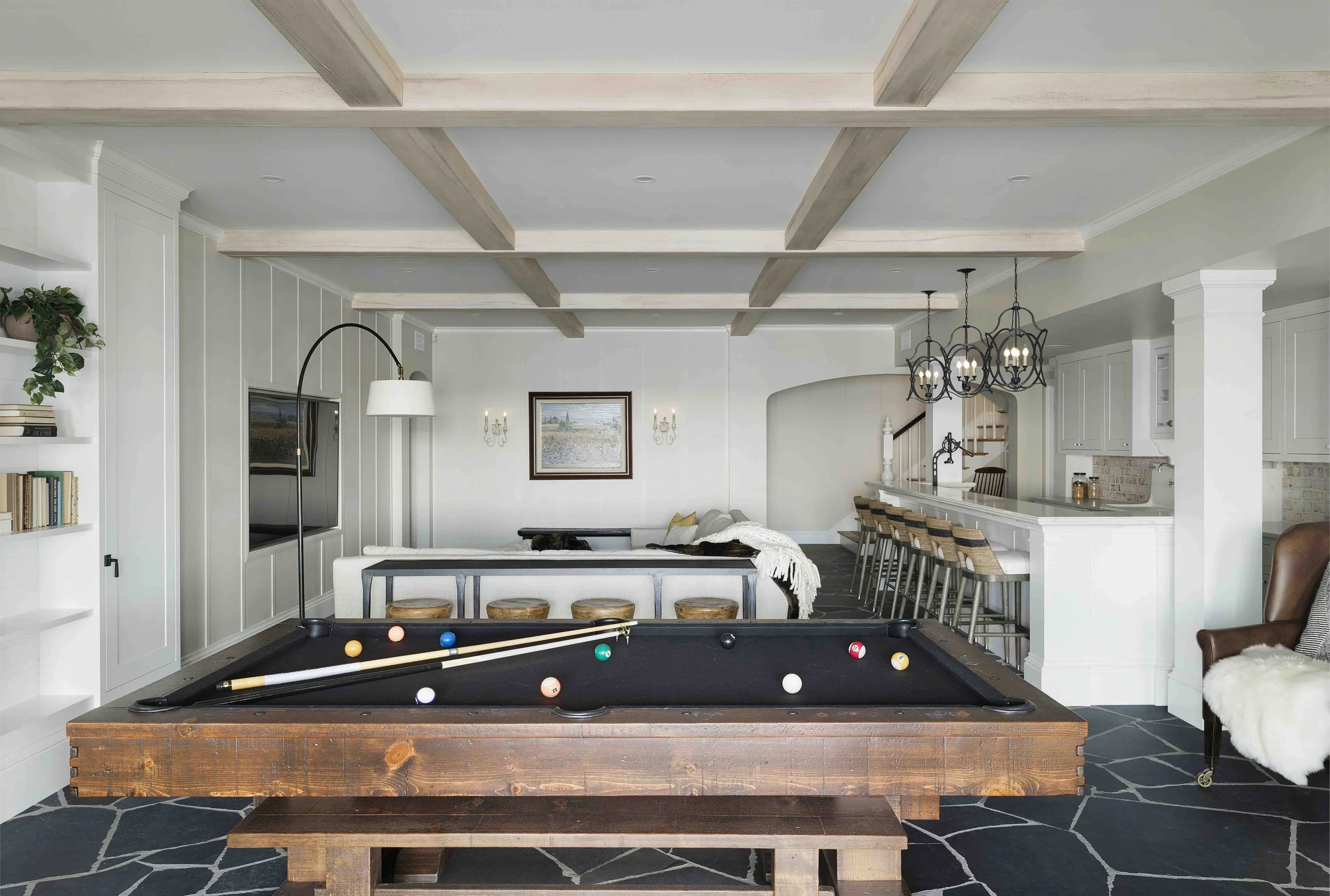 A recreation room with white walls, light wood floor ceiling, pool table and built-in bar