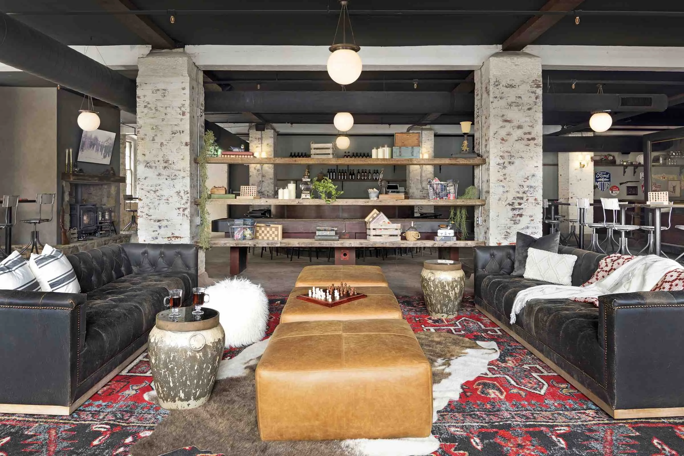 A lounge area with dark wooden ceiling, black leather couches and brown leather ottomans