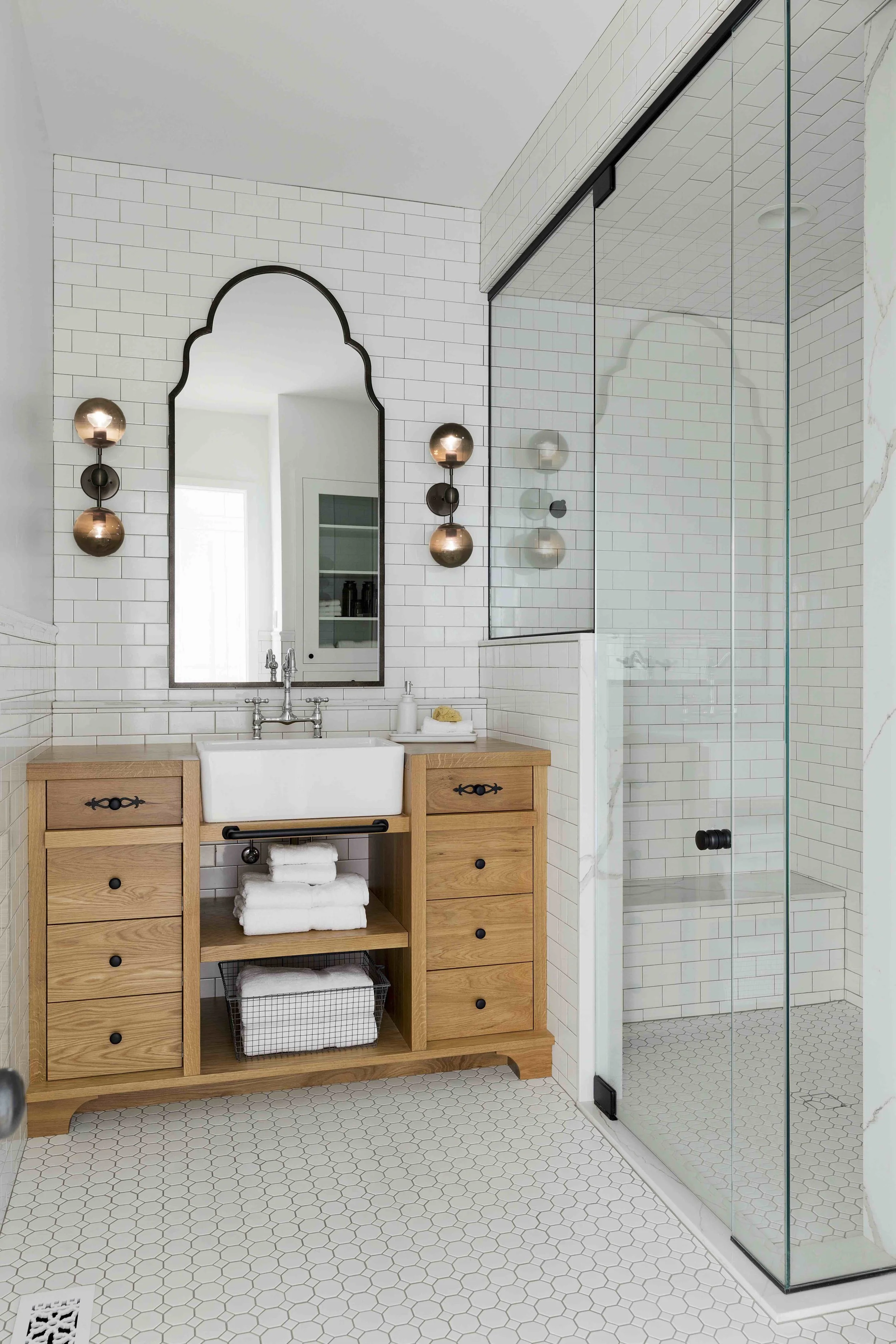 A modern black and white bathroom with white wall tiles, black trimmed wall mirror, glass shower and natural wood vanity