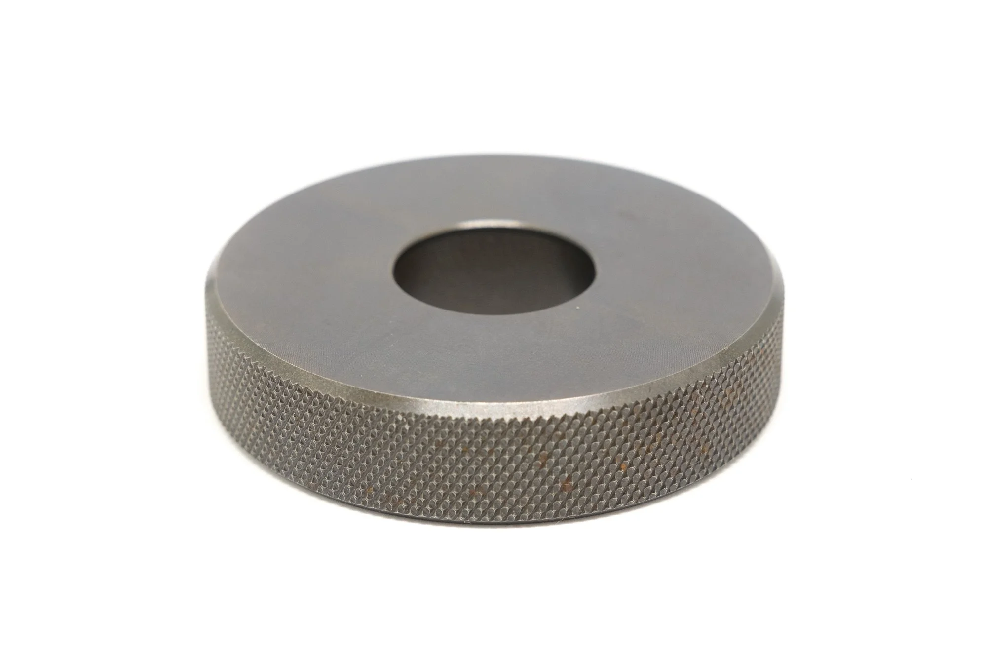 Metal knurled circular knob or dial with a central hole, isolated on white background.