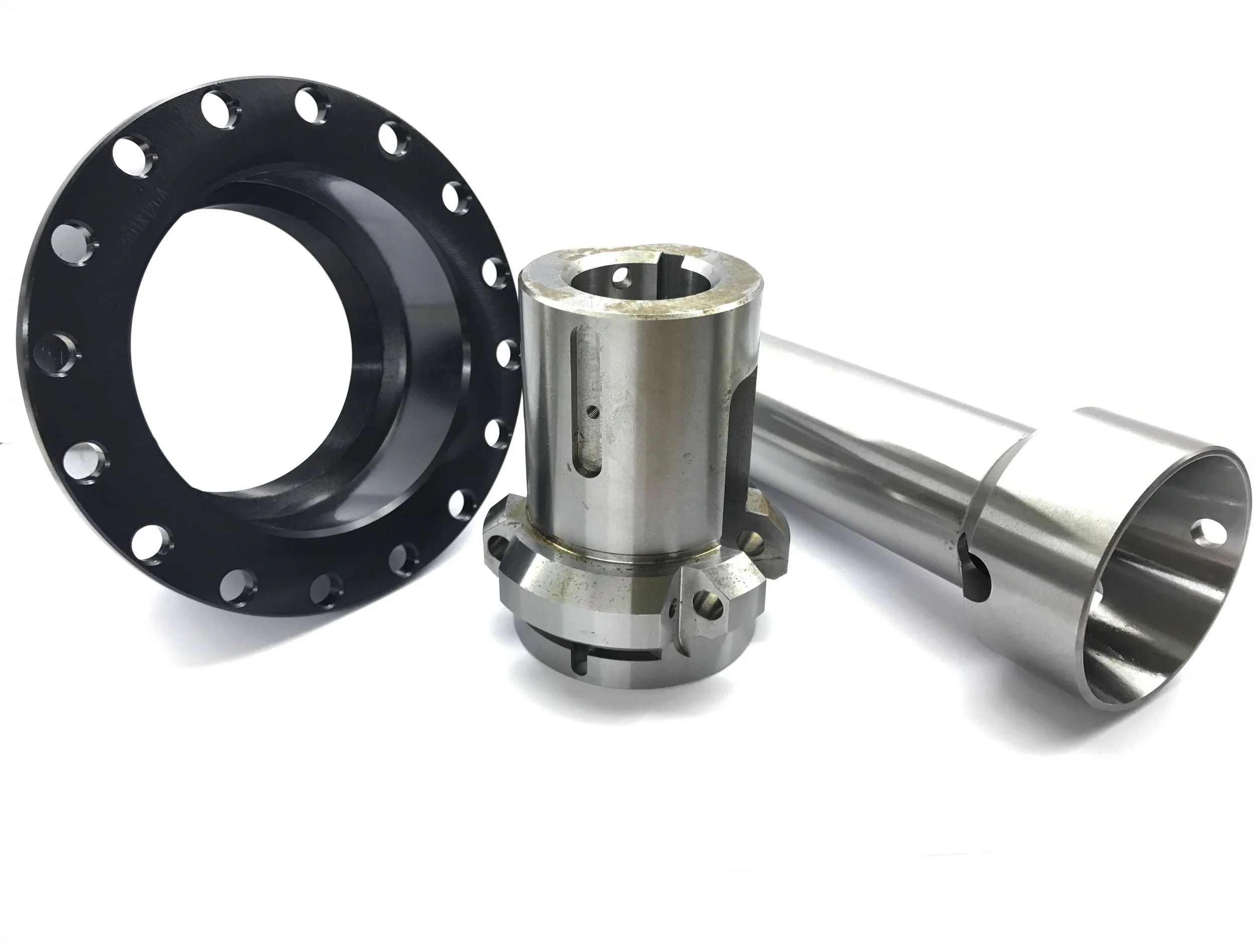 Metal mechanical parts including a black circular flange, a silver cylindrical hub with geometric cuts, and a shiny silver tube, arranged on a white background.