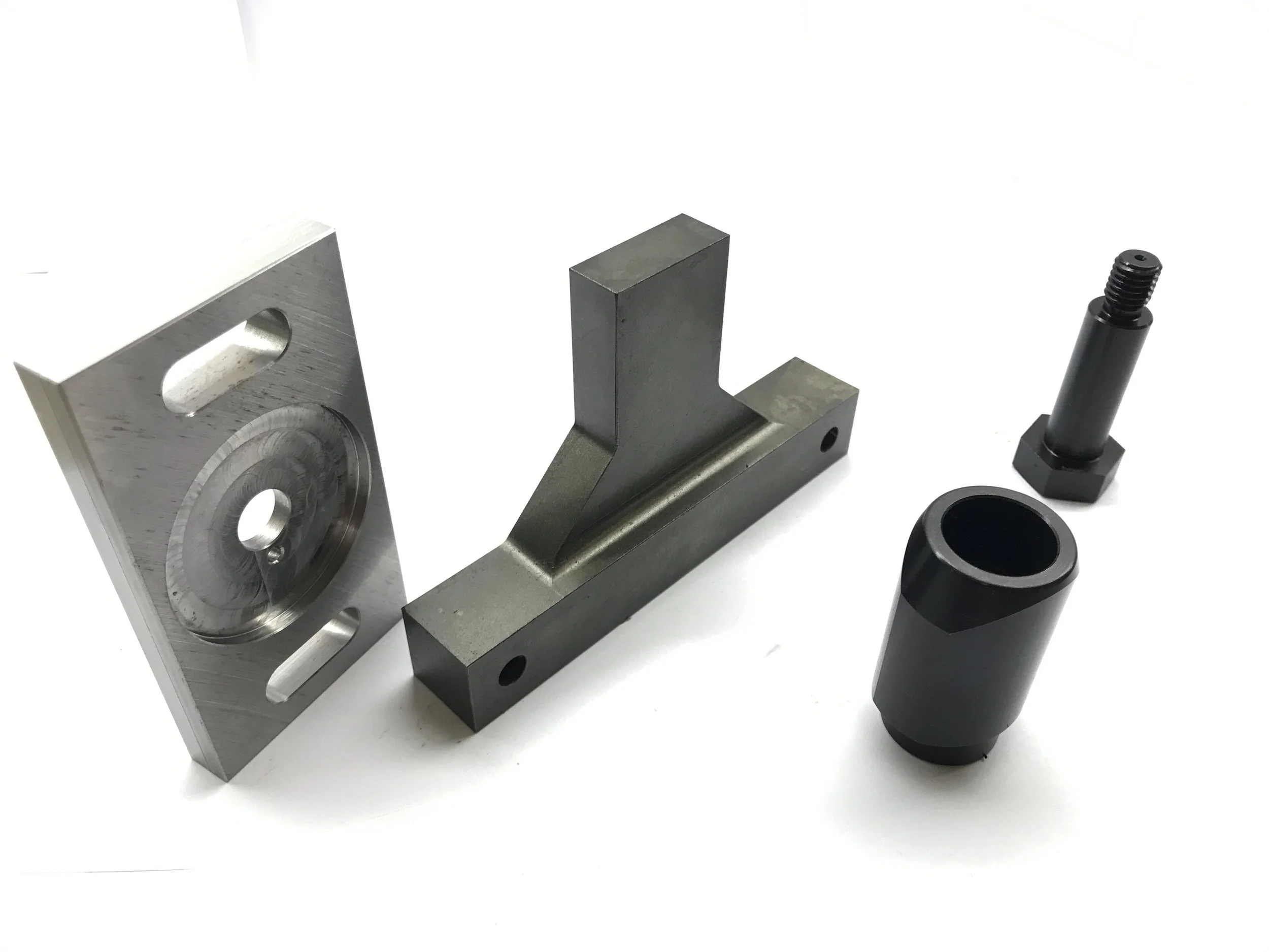Various metal machine parts including a rectangular block with a vertical extension, a cylindrical piece, and a bolt.