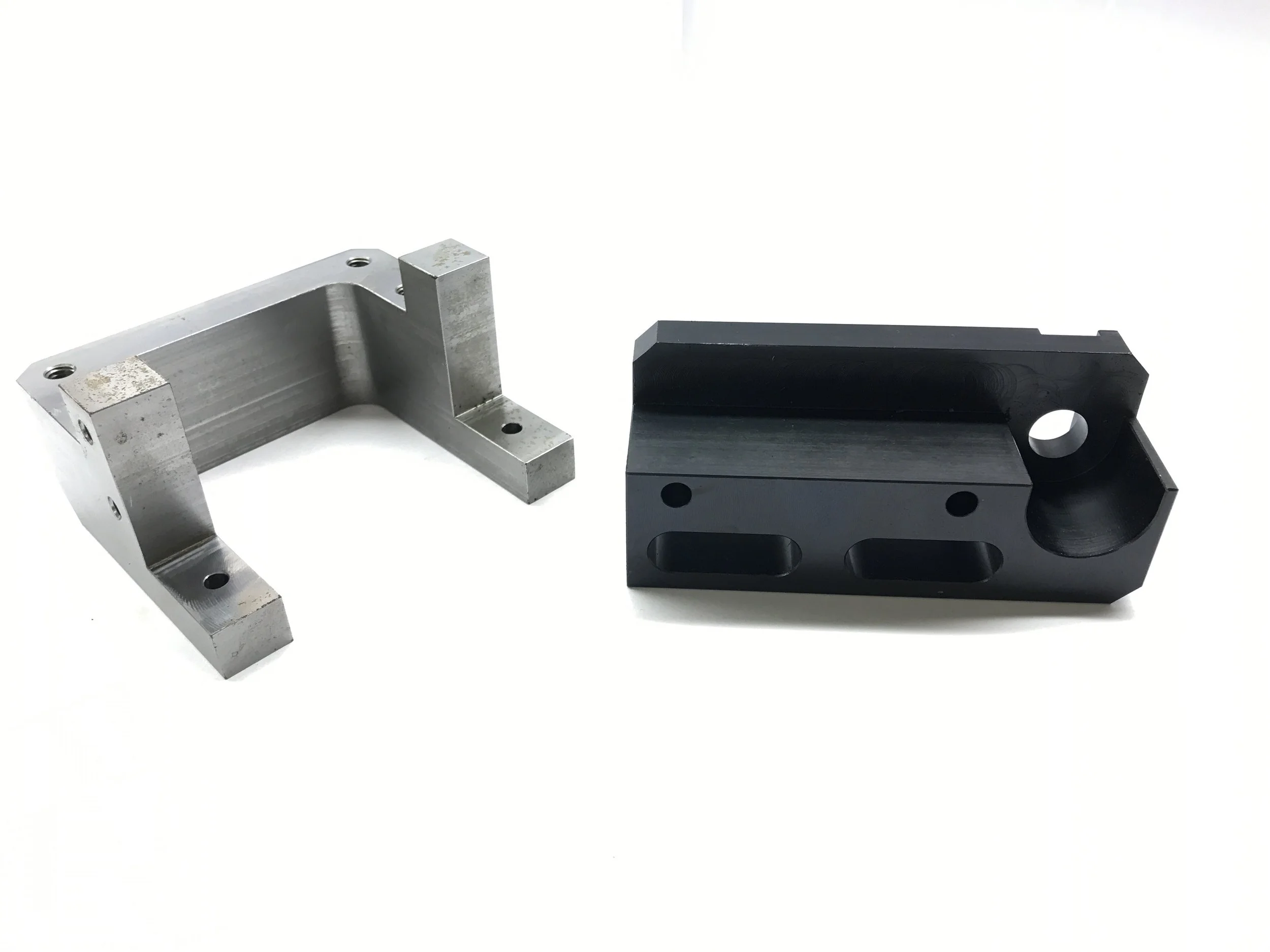 Two metal mechanical parts, one silver and one black, placed on a white surface.