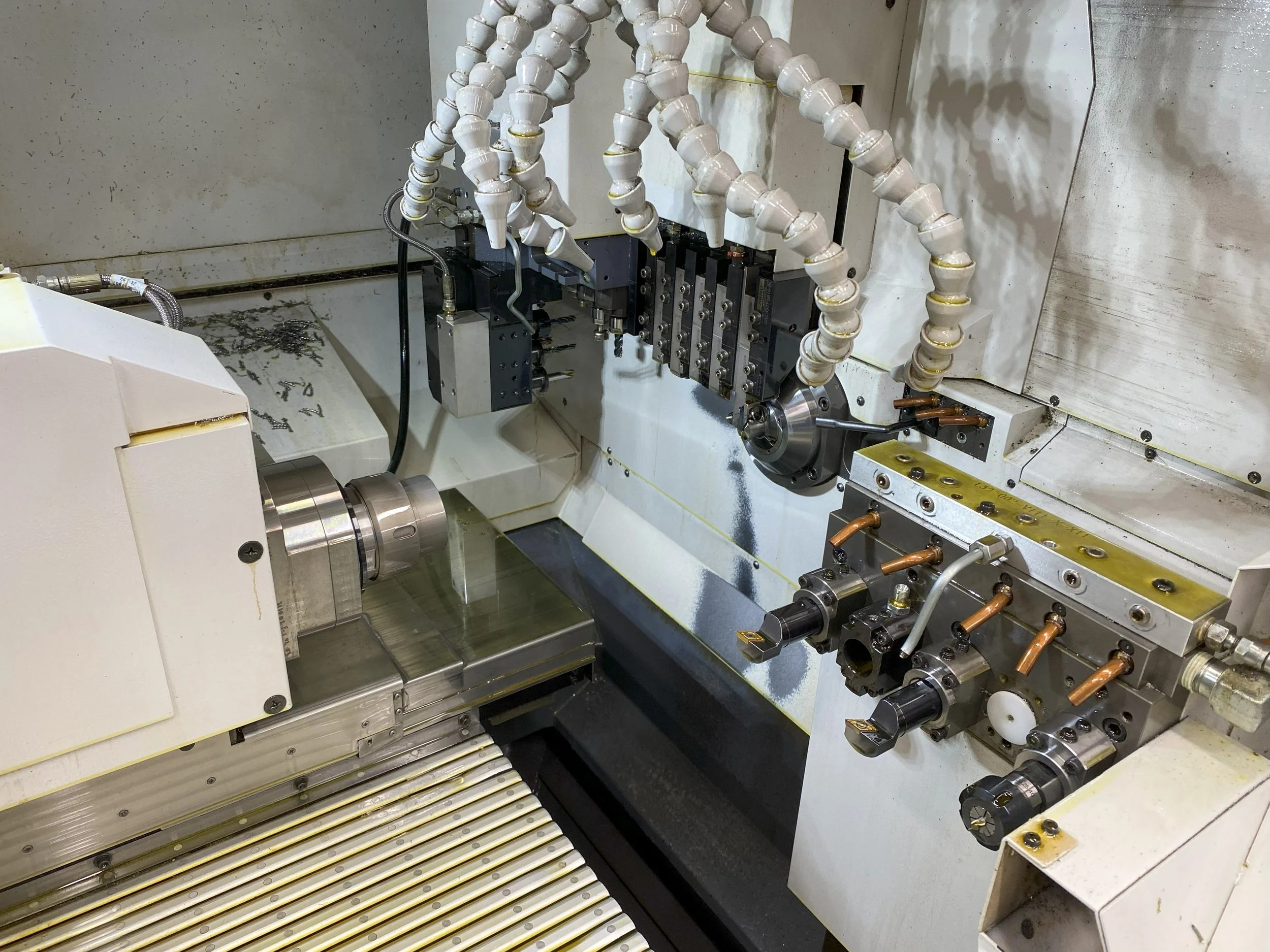 Close-up of a precision CNC machine with various metal components, coolant hoses, and a rotating spindle.