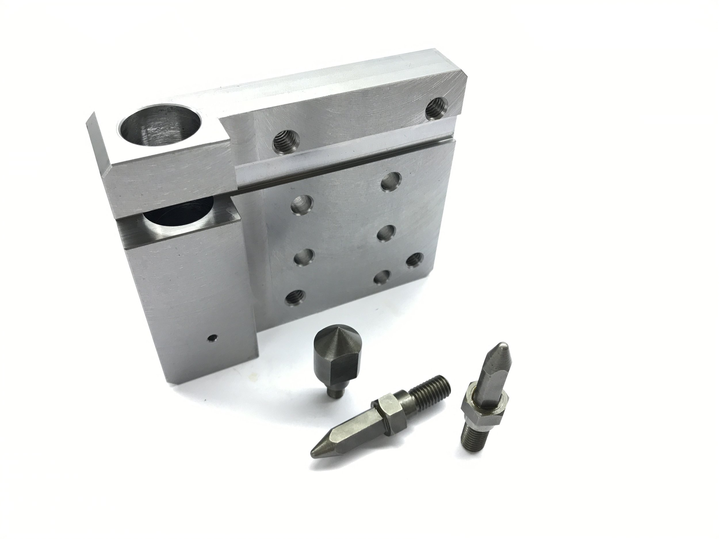 Metal machining fixture with three different metal screws and a pin placed in front of it on a white background.