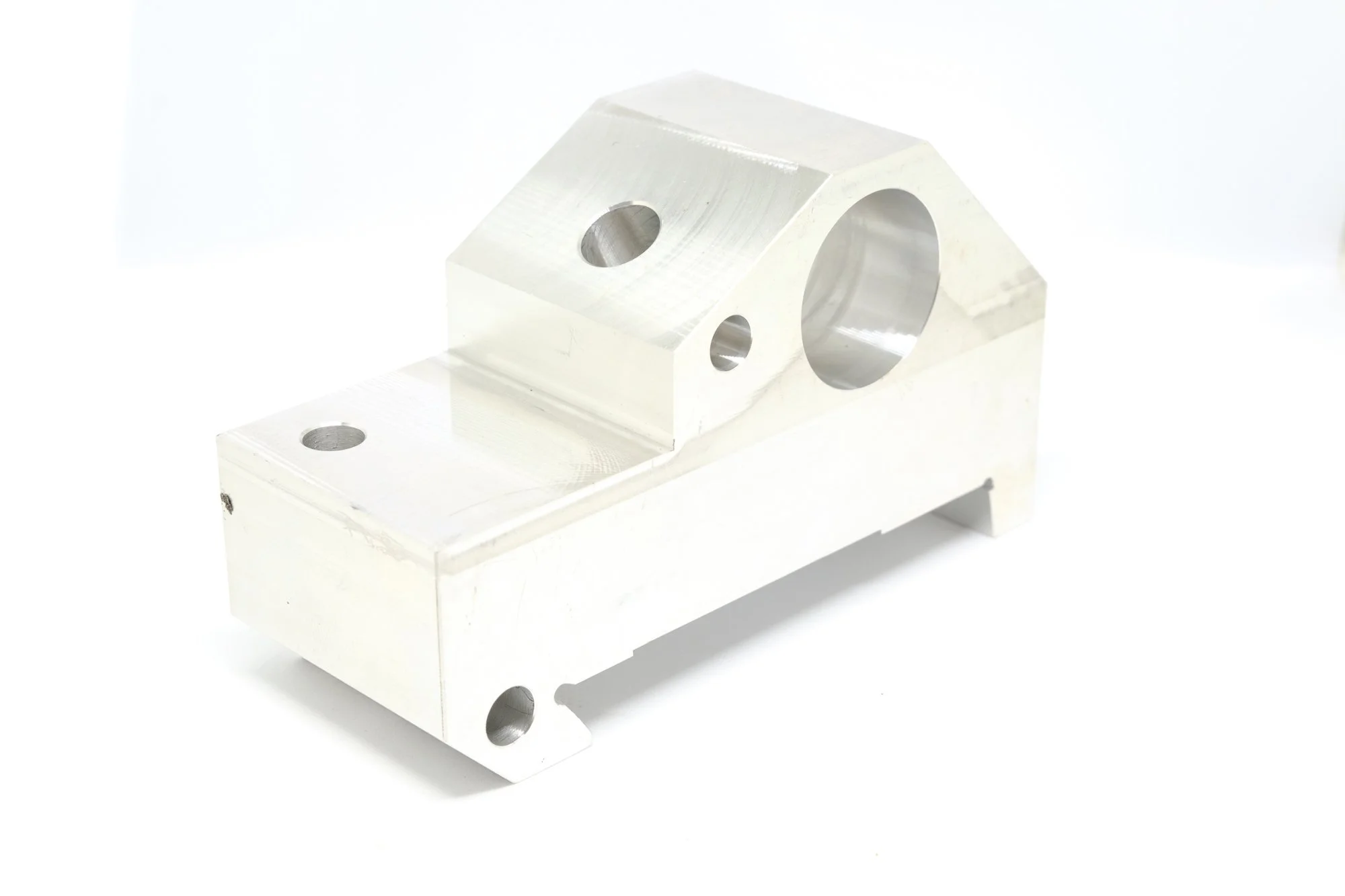 Silver machined metal part with multiple holes, rectangular base, and angled top surface, isolated on white background.
