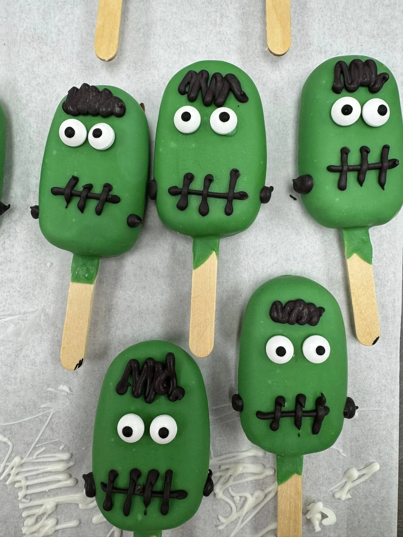 Green monster-shaped Cakesicles with white eyes and black pupils, black hair, and black stitched mouths