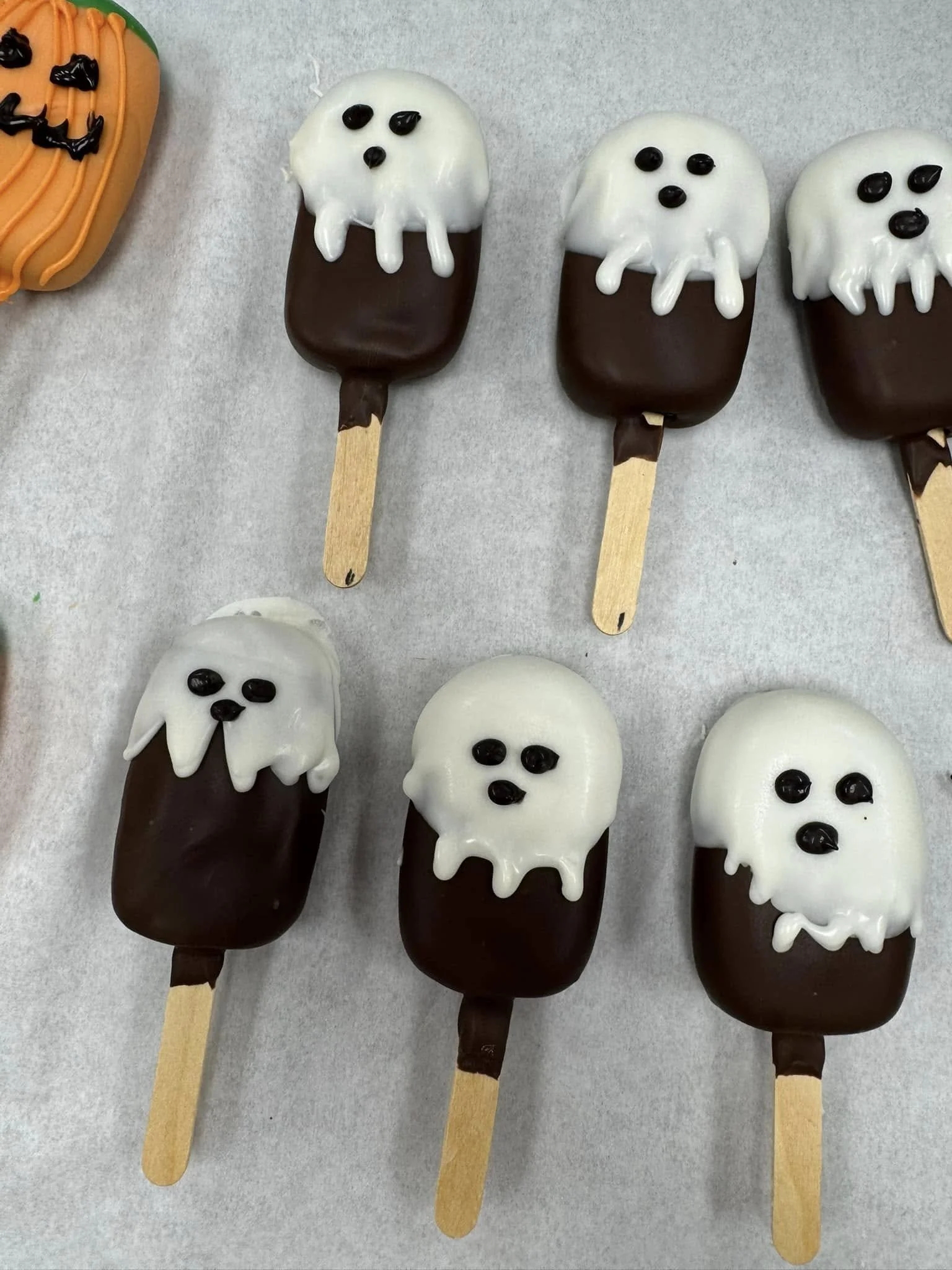 Halloween-themed ghost Cakesicles, decorated with white and dark chocolate and small black candy eyes