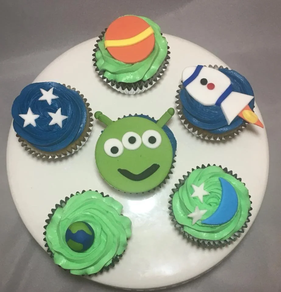 Cupcakes decorated with outer space-themed icing, including planets, astronauts, and an alien.