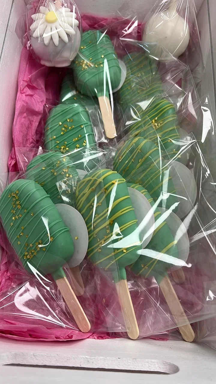 A box of green chocolate-covered Cakesicles with yellow drizzle and gold star sprinkles
