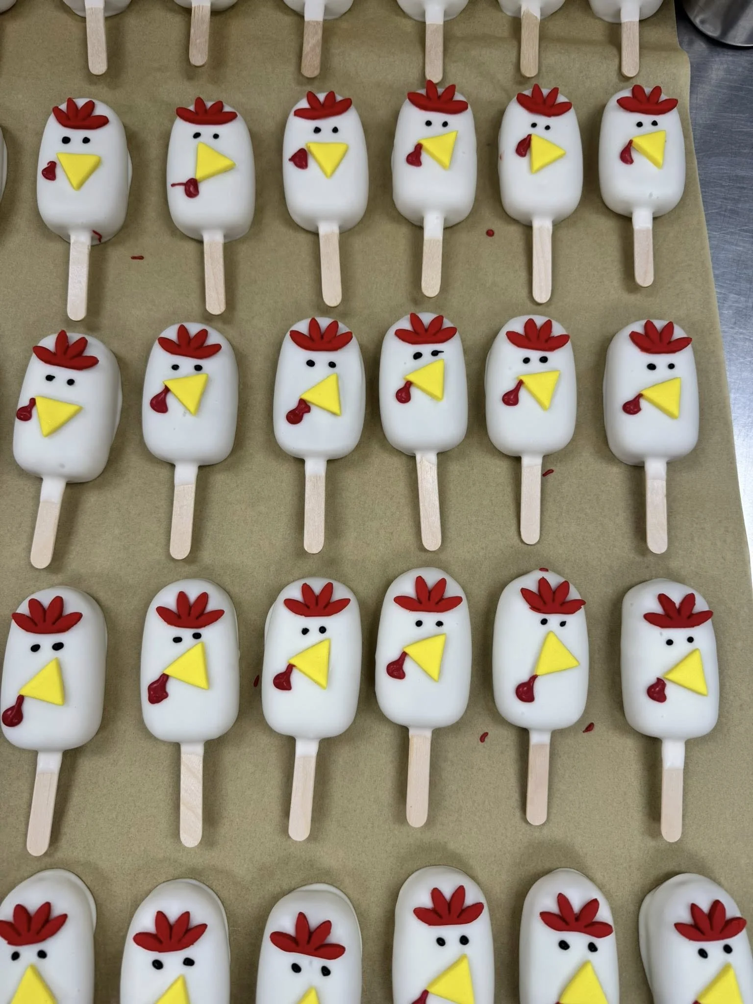 Cakesicles decorated to look like chickens with red combs, yellow beaks, and small black eyes