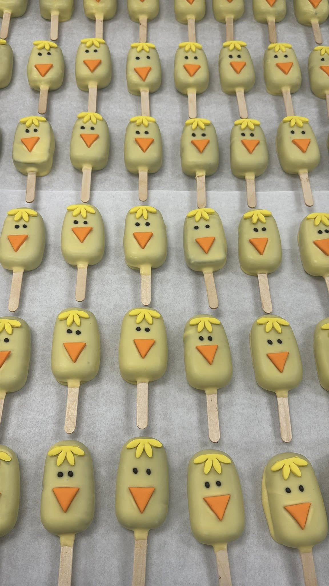 Easter chick-themed Cakesicles decorated to resemble cute chicks with yellow bodies, orange beaks, and small black eyes