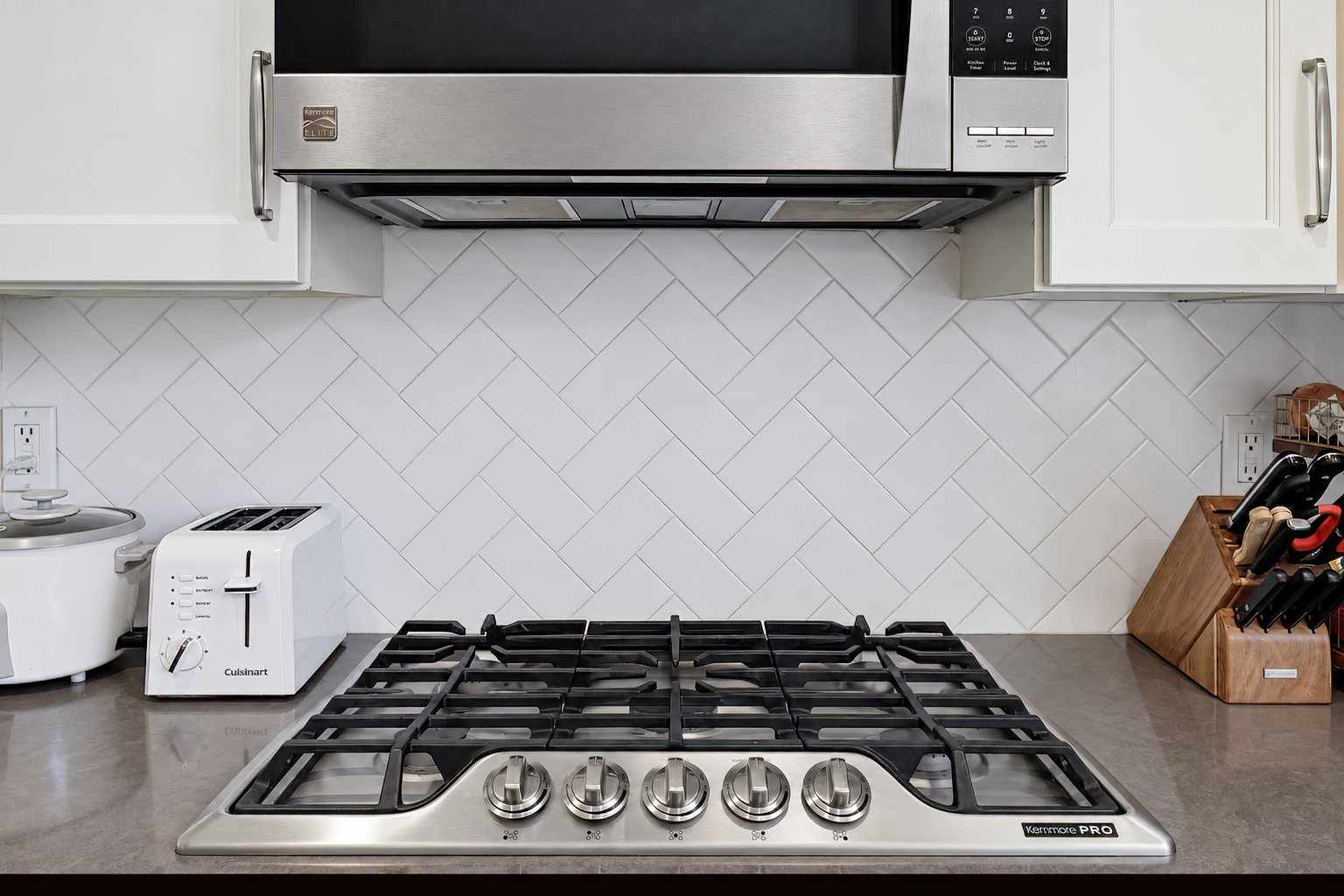 Gas cooktop below a stainless-steel microwave and white tile backsplash.