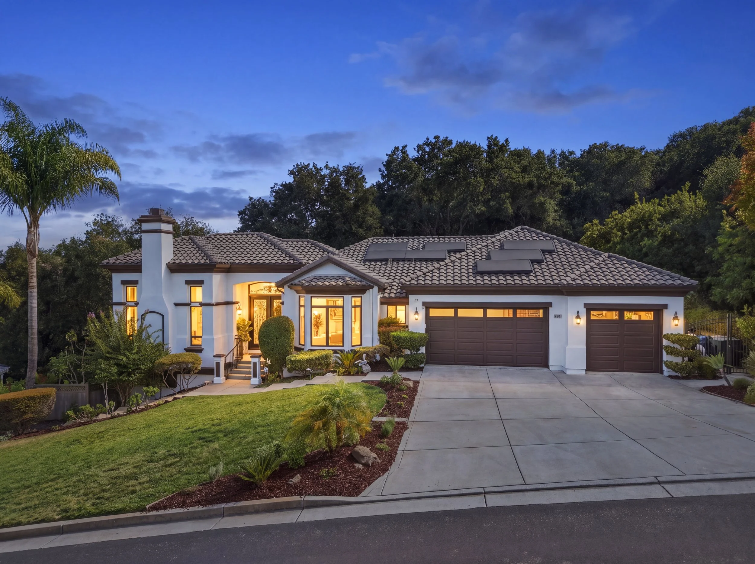 Gilroy home at twilight with illuminated windows, garage, and landscaping.