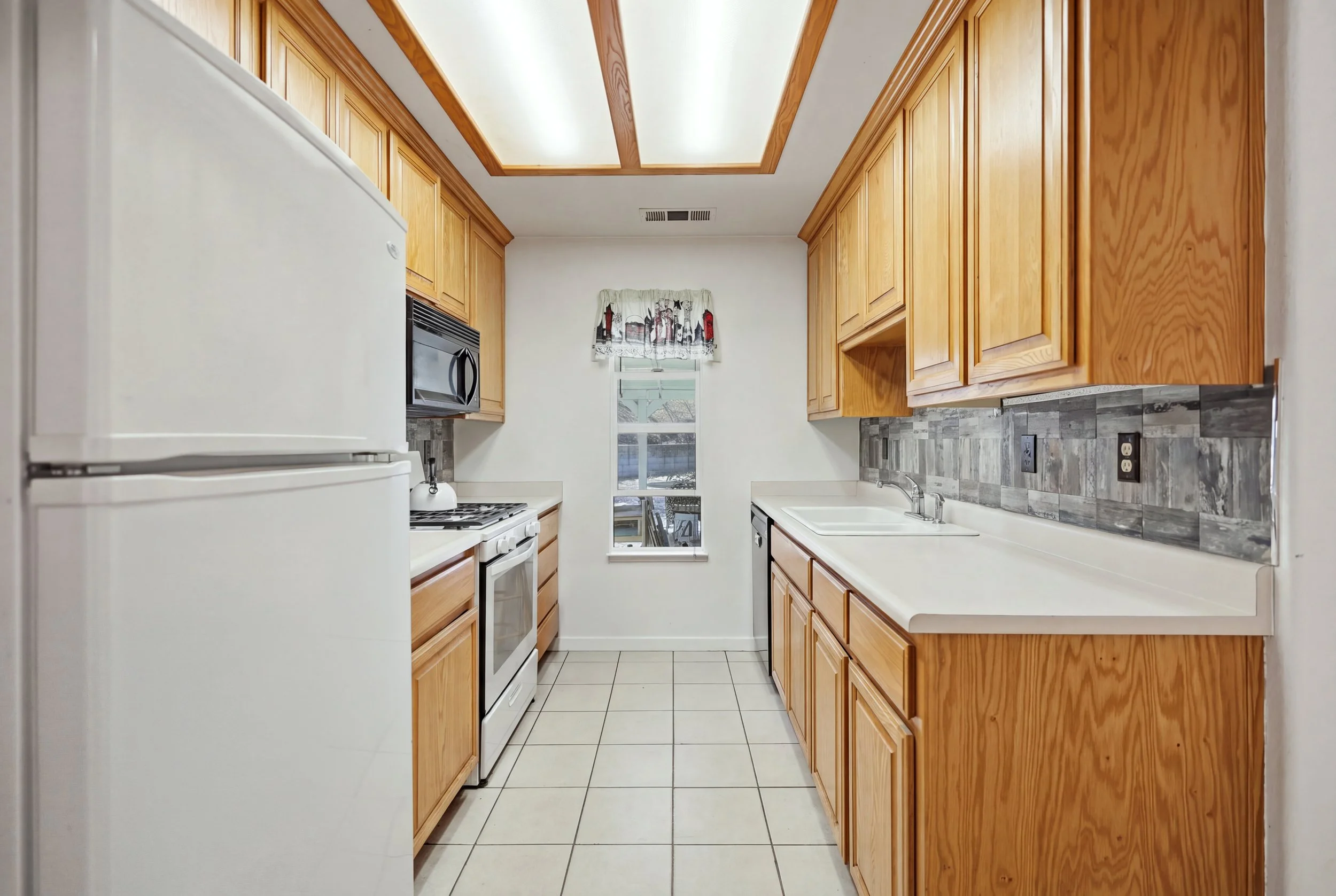 Galley kitchen with wood cabinets, tile floor, and ceiling light panels.