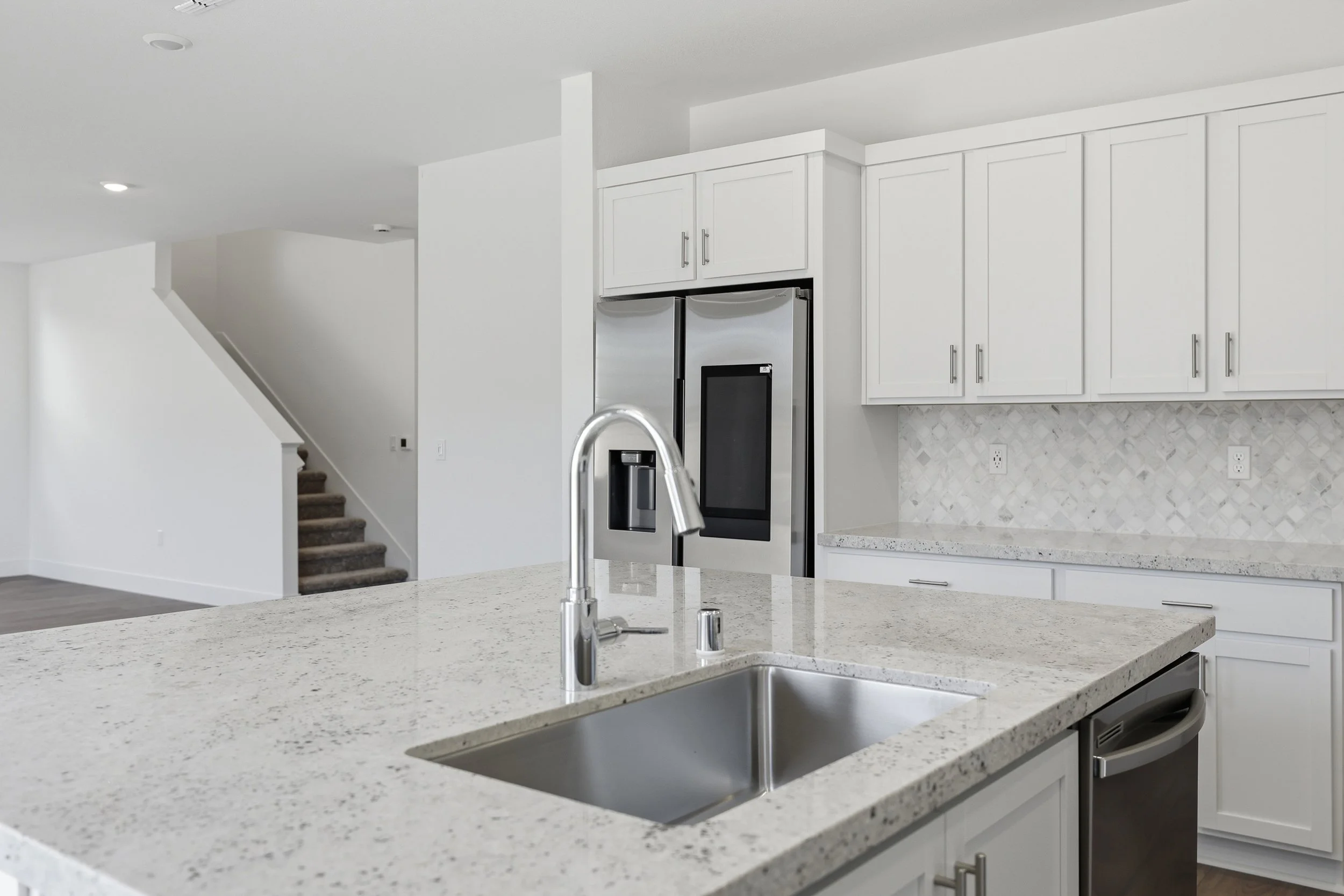 Kitchen sink on an island facing white cabinets and stainless-steel refrigerator.