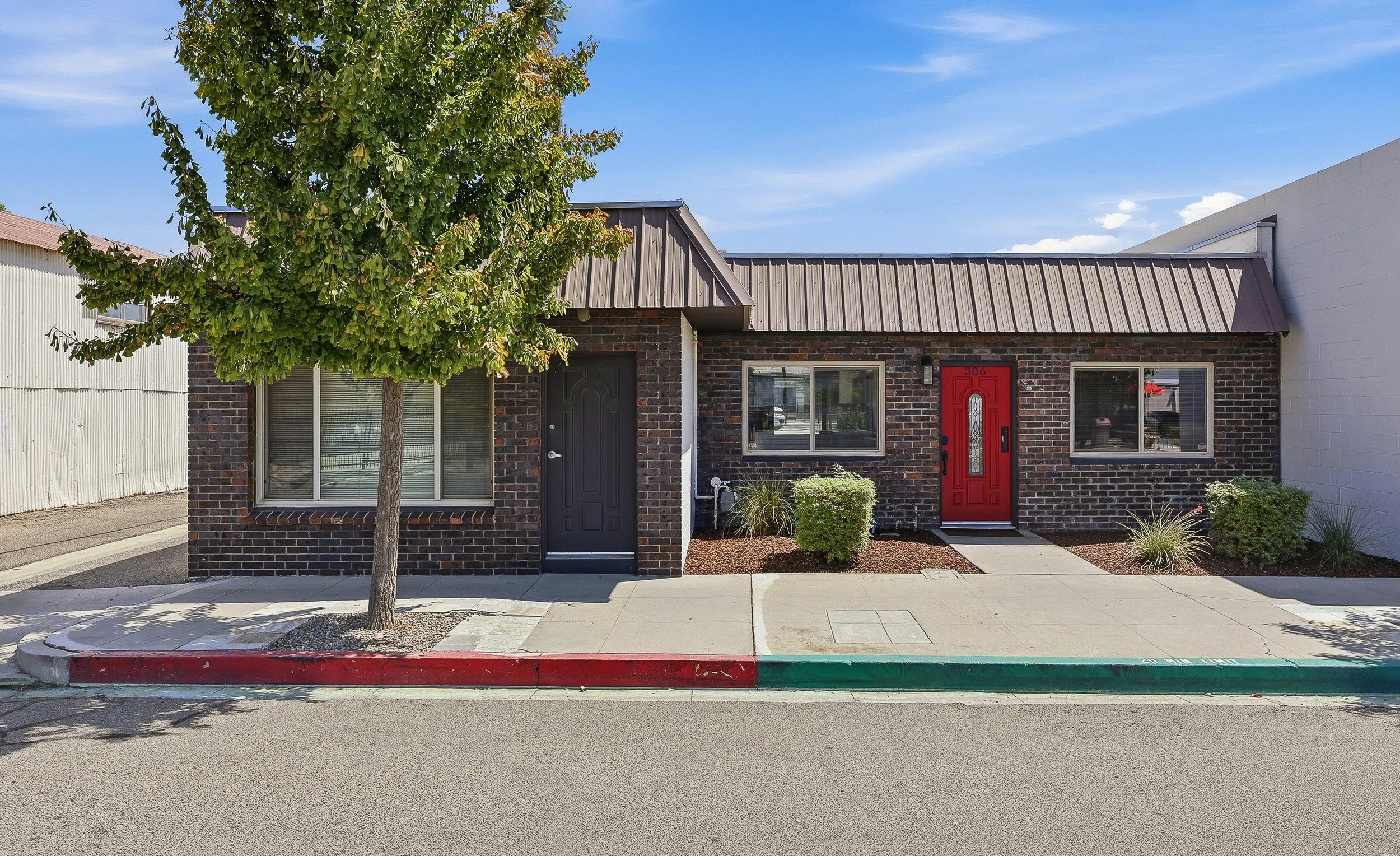 Visalia building with dark brick facade, red front door, and sidewalk tree.