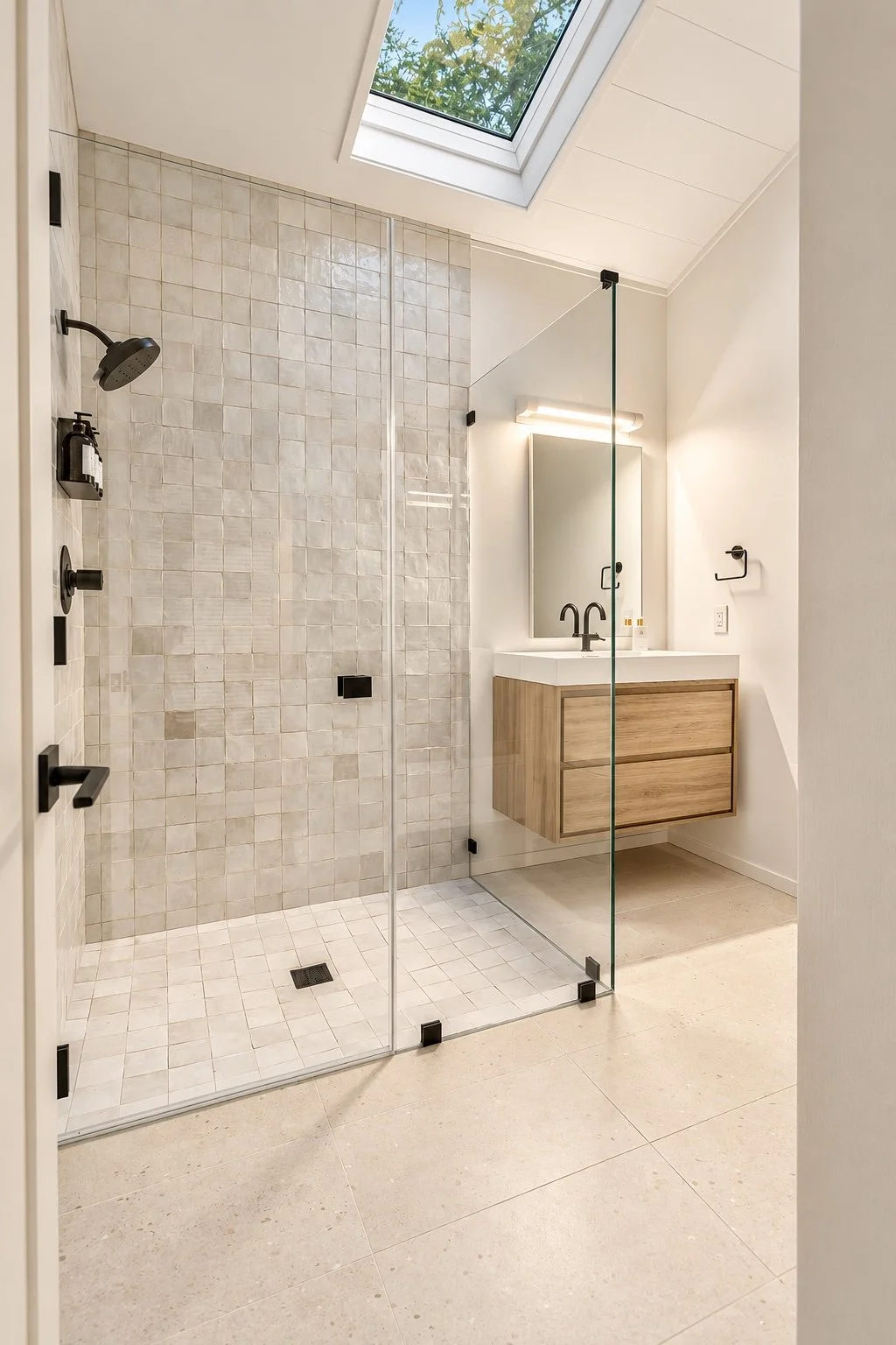 Carmel bathroom with a glass-enclosed tiled shower, floating wood vanity, black fixtures, and a skylight.