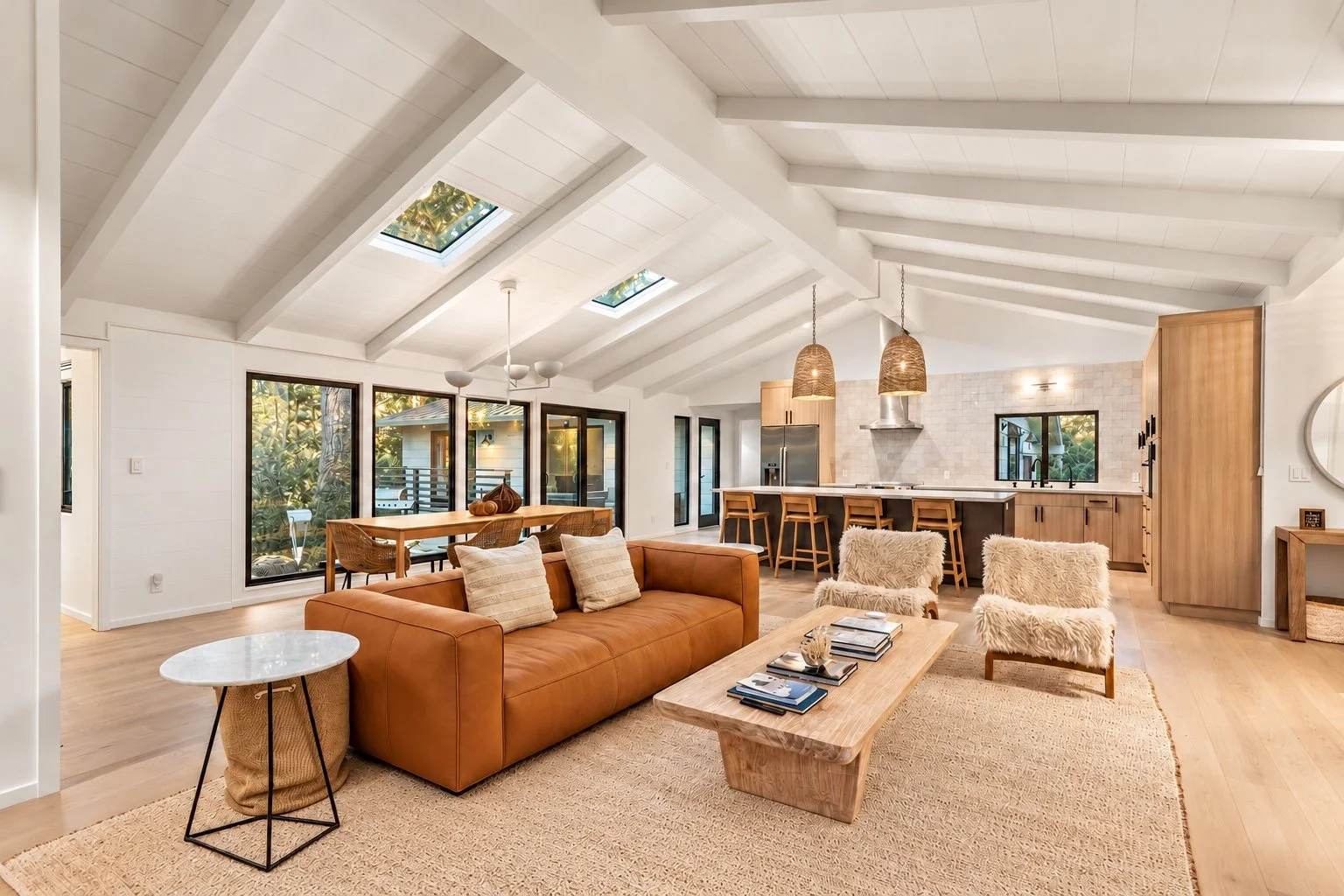 Open-plan Carmel living room with a tan leather sofa, vaulted white beams, skylights, and a wood-cabinet kitchen.