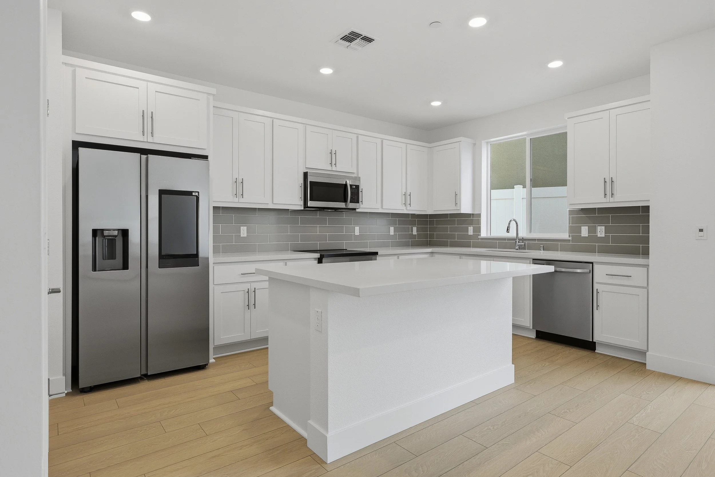 White kitchen with island, stainless-steel appliances, and recessed lighting.