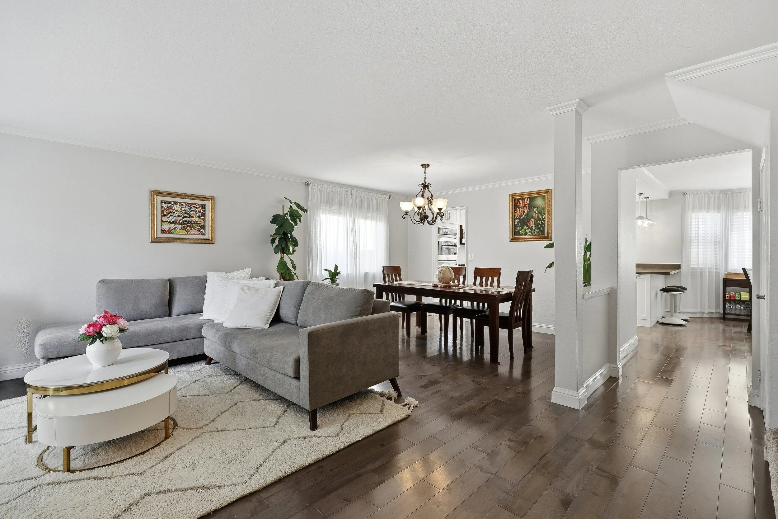 Open living and dining room with gray sofa, wood flooring, and white walls.