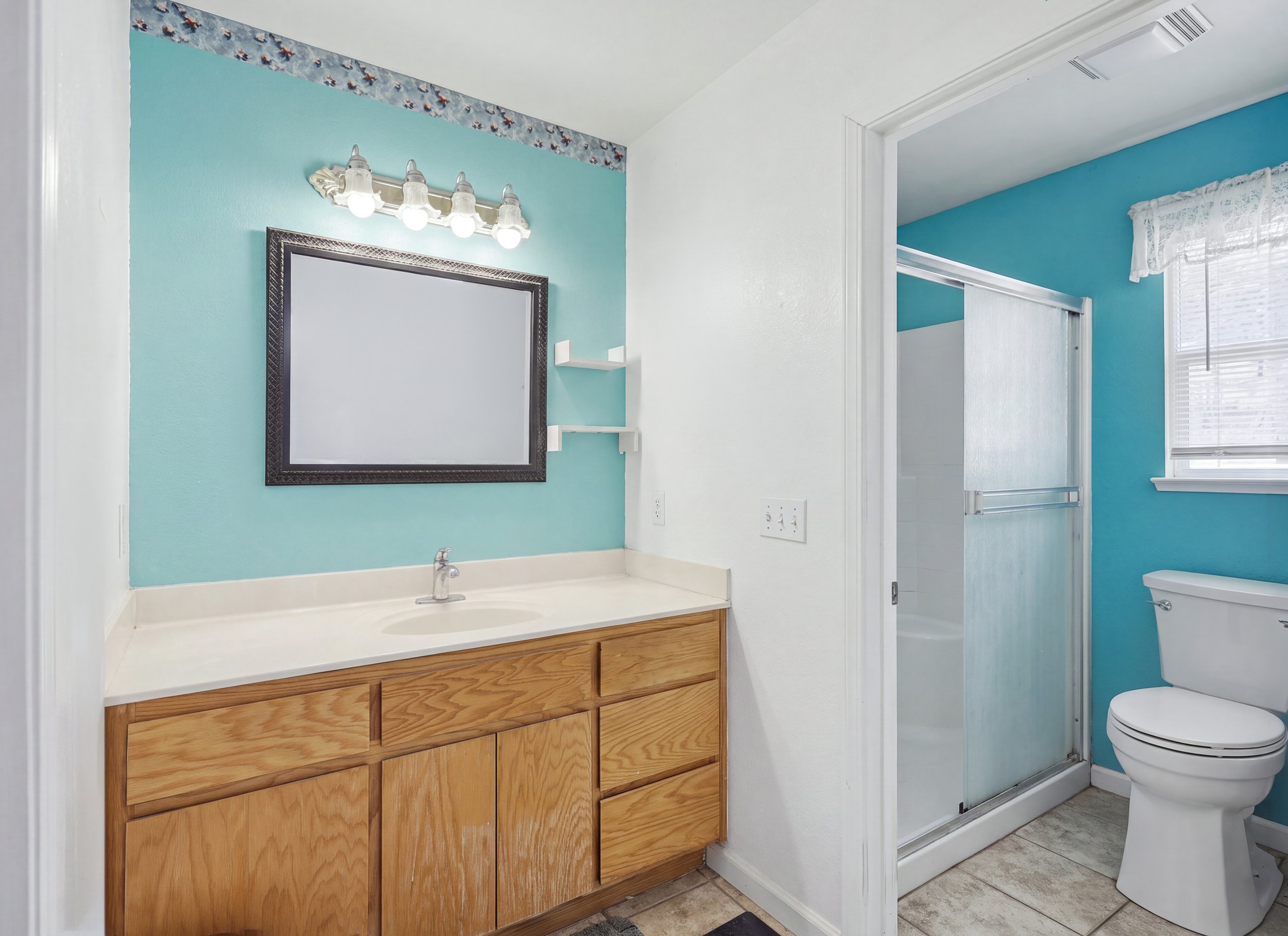 Bathroom with wood vanity, mirror, turquoise walls, and shower enclosure.