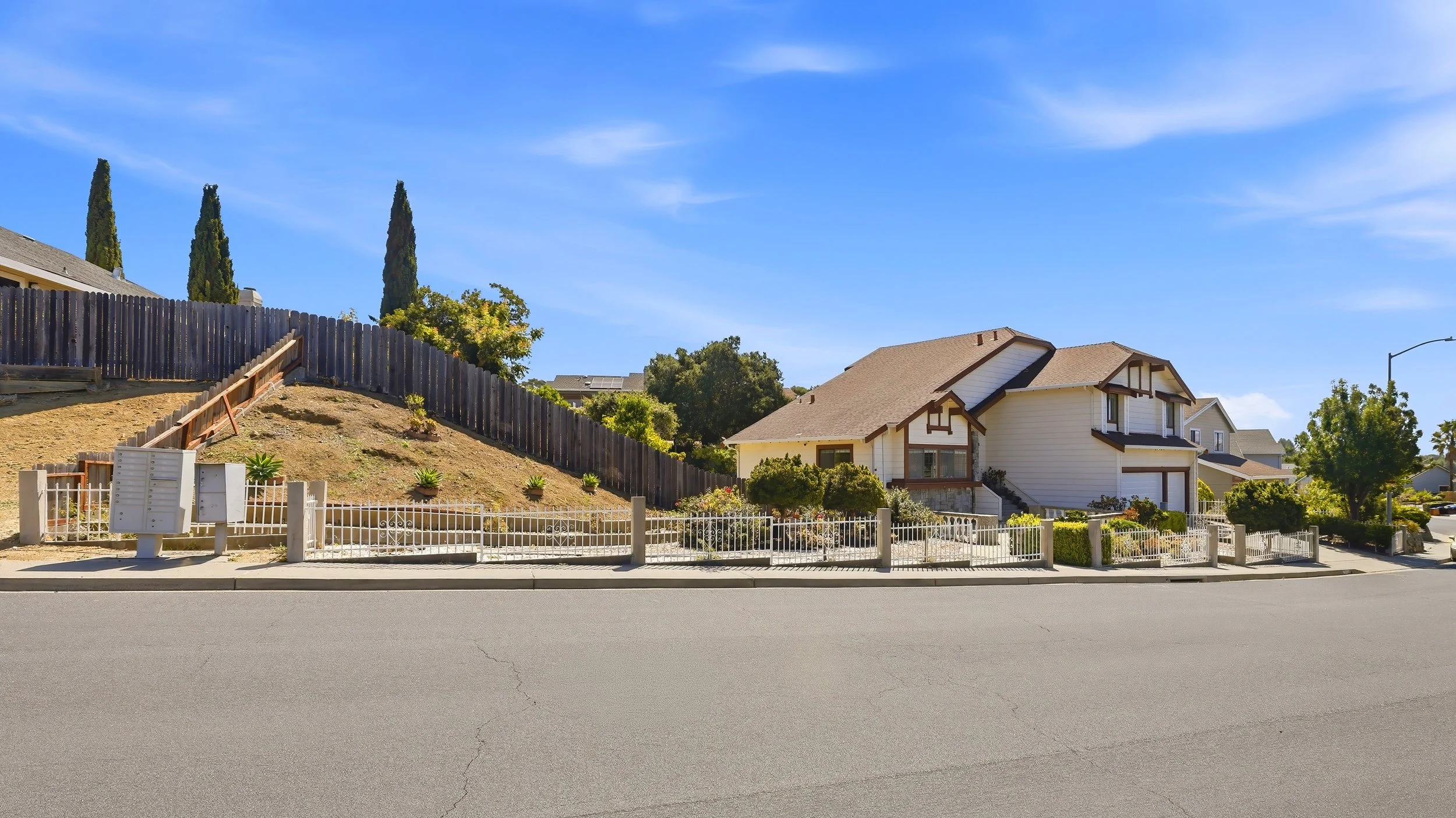 Residential neighborhood with white house, trees, and a clear blue sky.