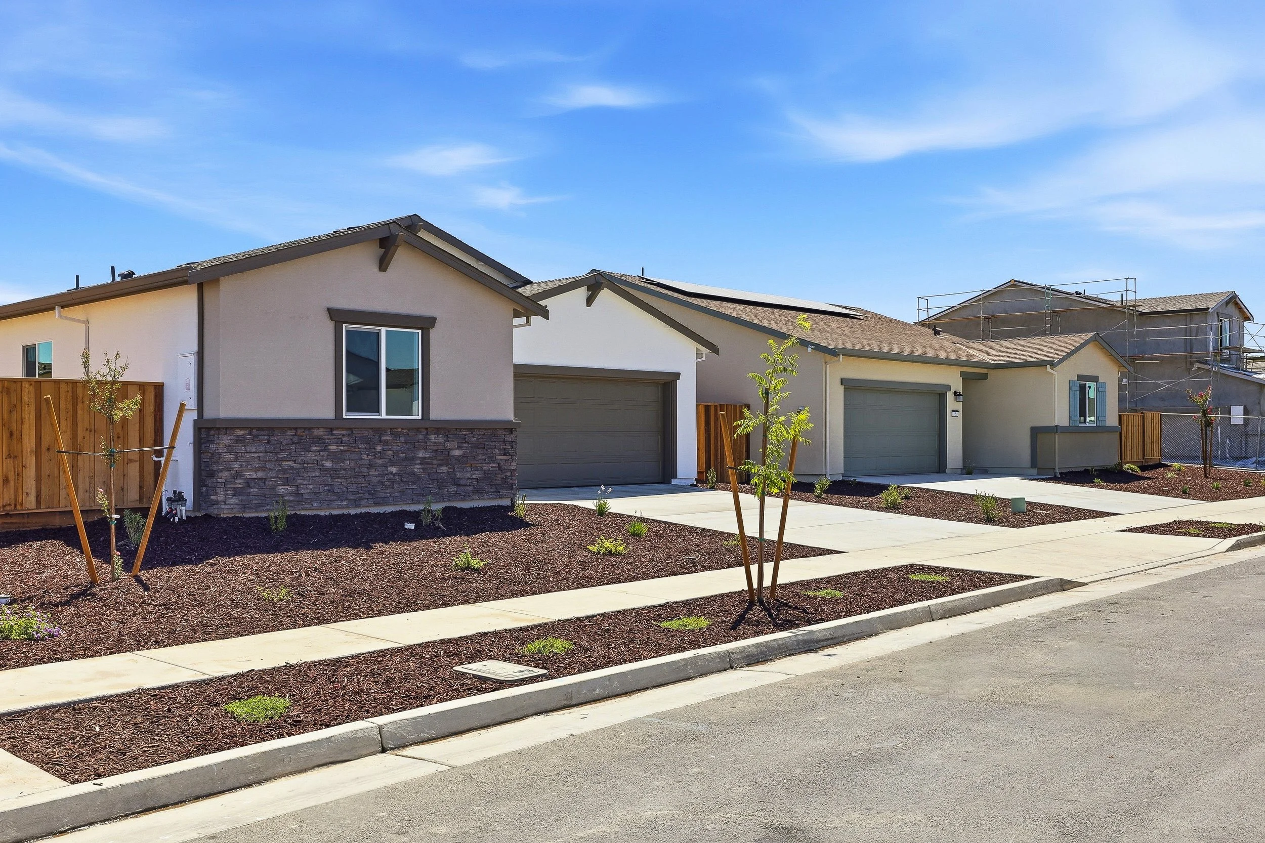 A row of newly built houses with front yards, some with scaffolding, under a clear blue sky.