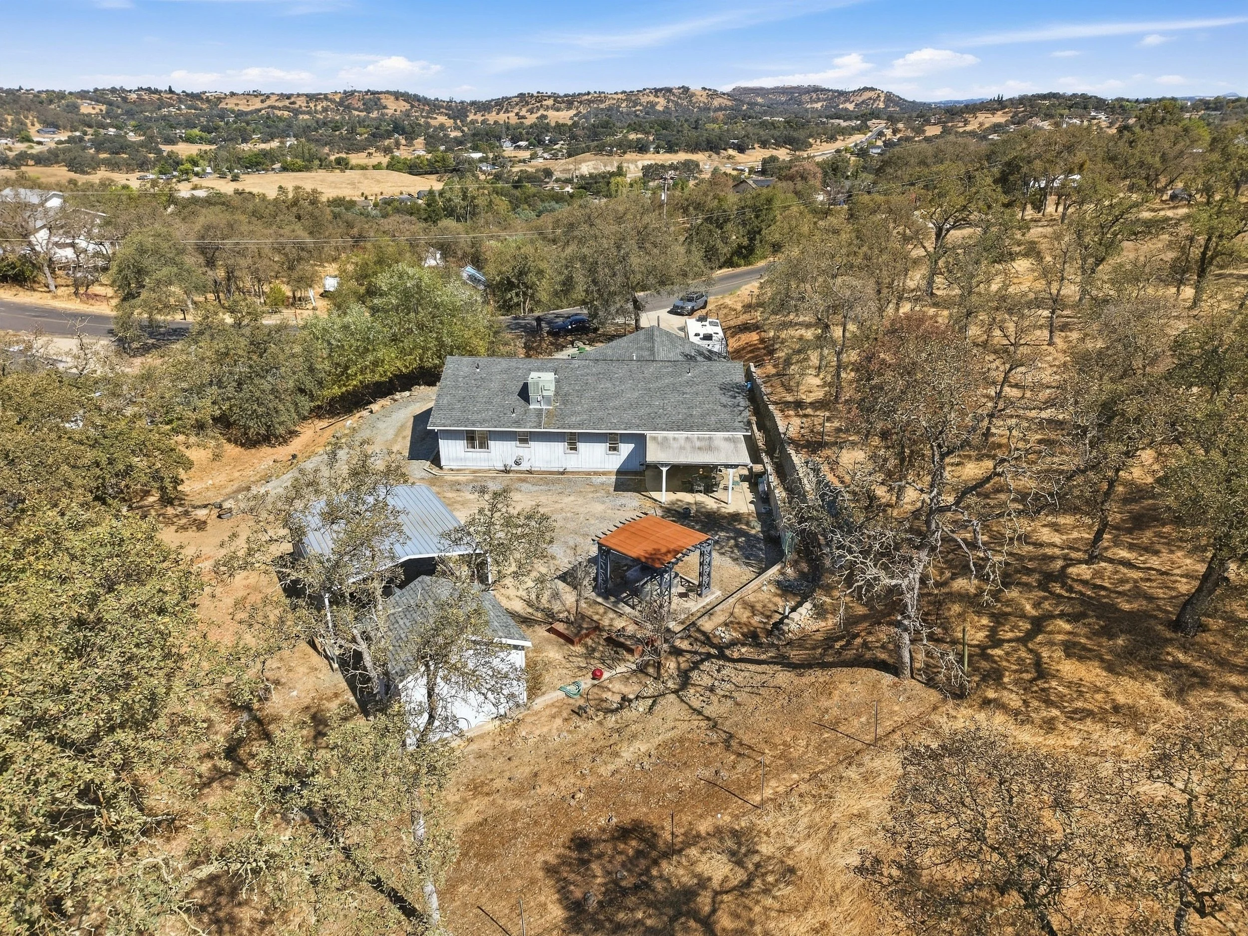 Aerial view of a rural home, outbuildings, and surrounding wooded landscape.